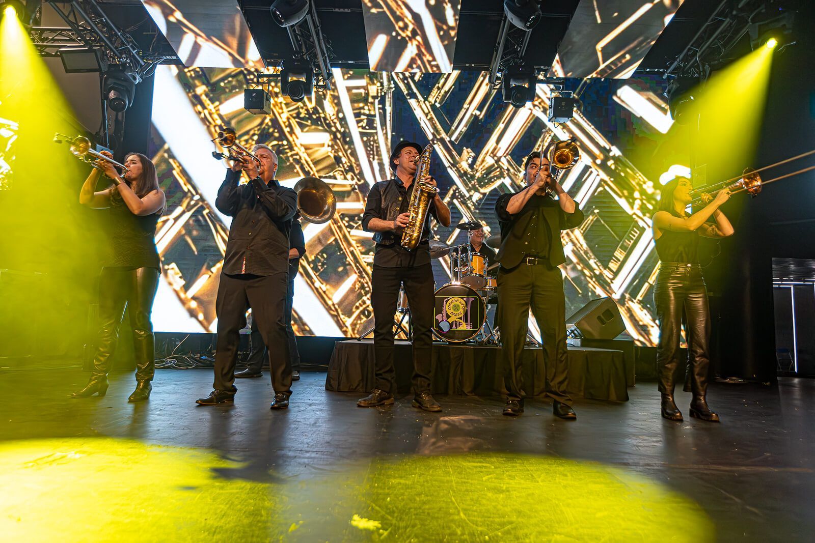 Band performing on stage under bright yellow and white lights with a geometric backdrop