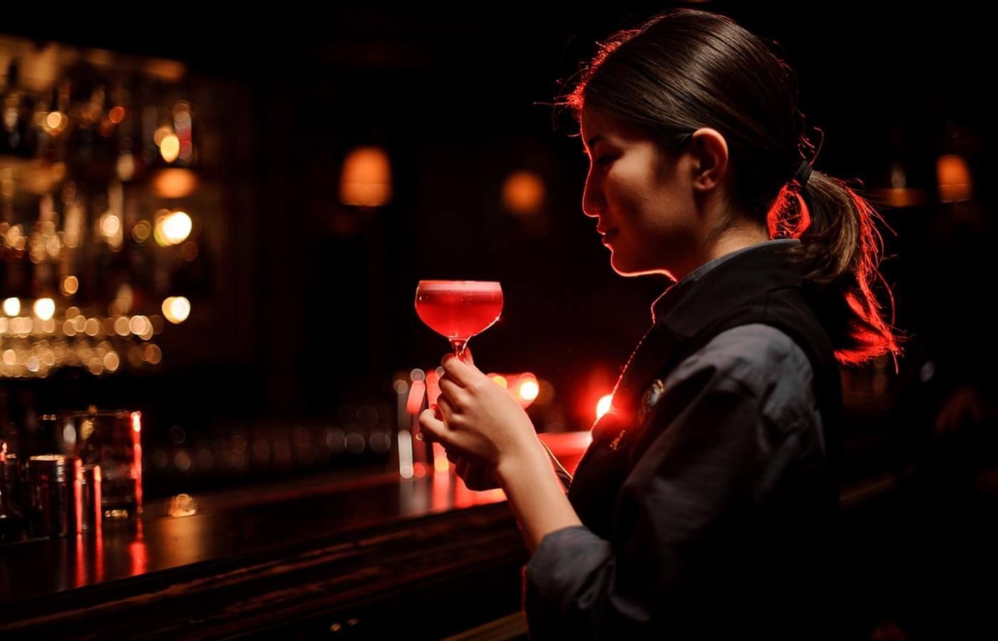 Woman at a dim bar holding a red cocktail glass, lit by warm red-orange lights