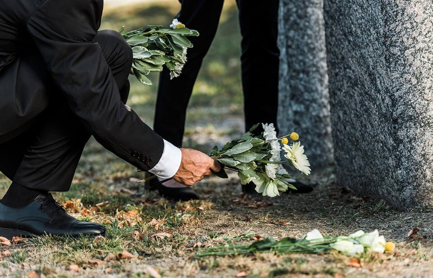 Person placing flowers at a gravestone outdoors
