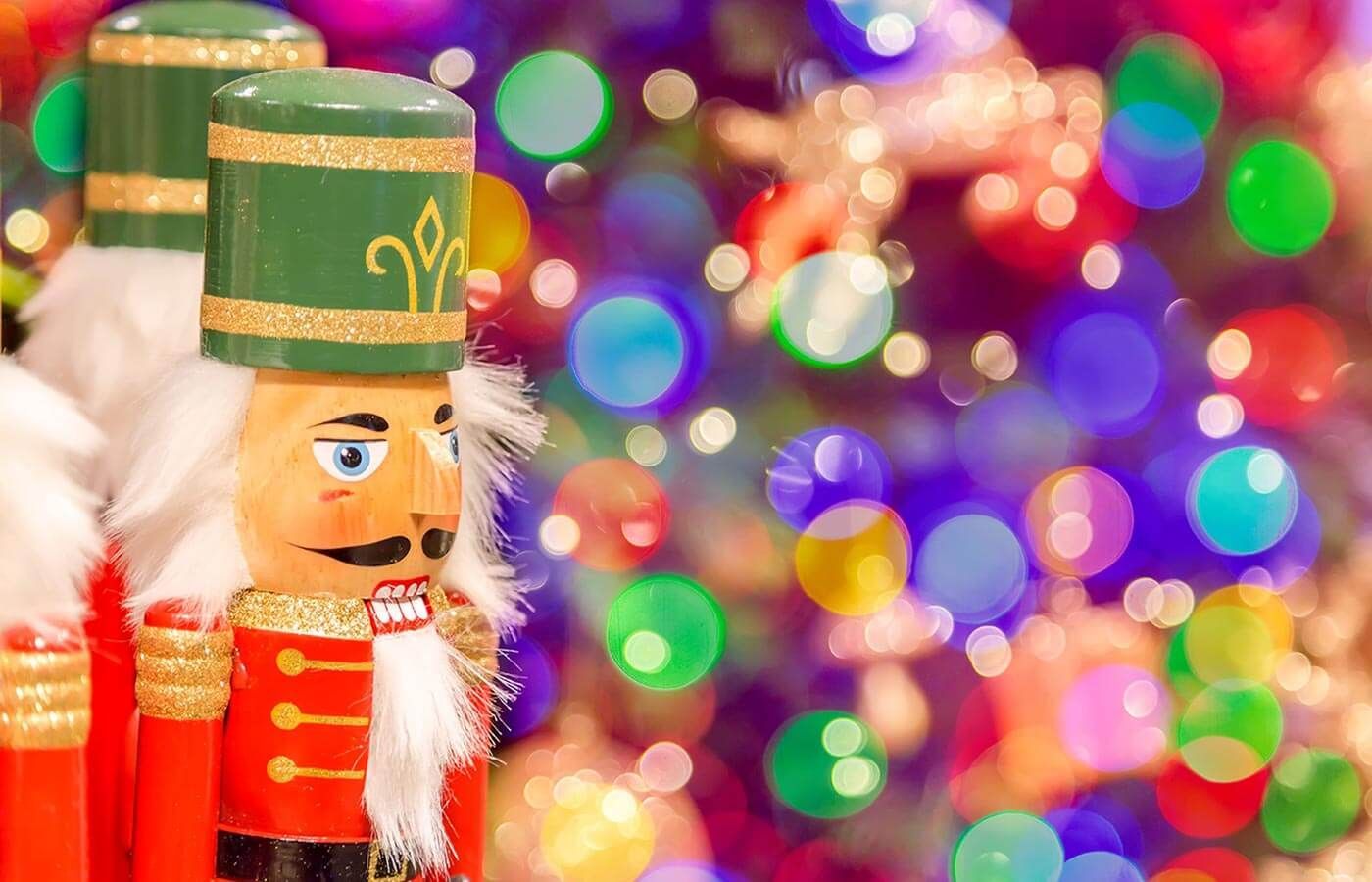 Toy soldier nutcracker in red and gold against a colorful blurred holiday lights background