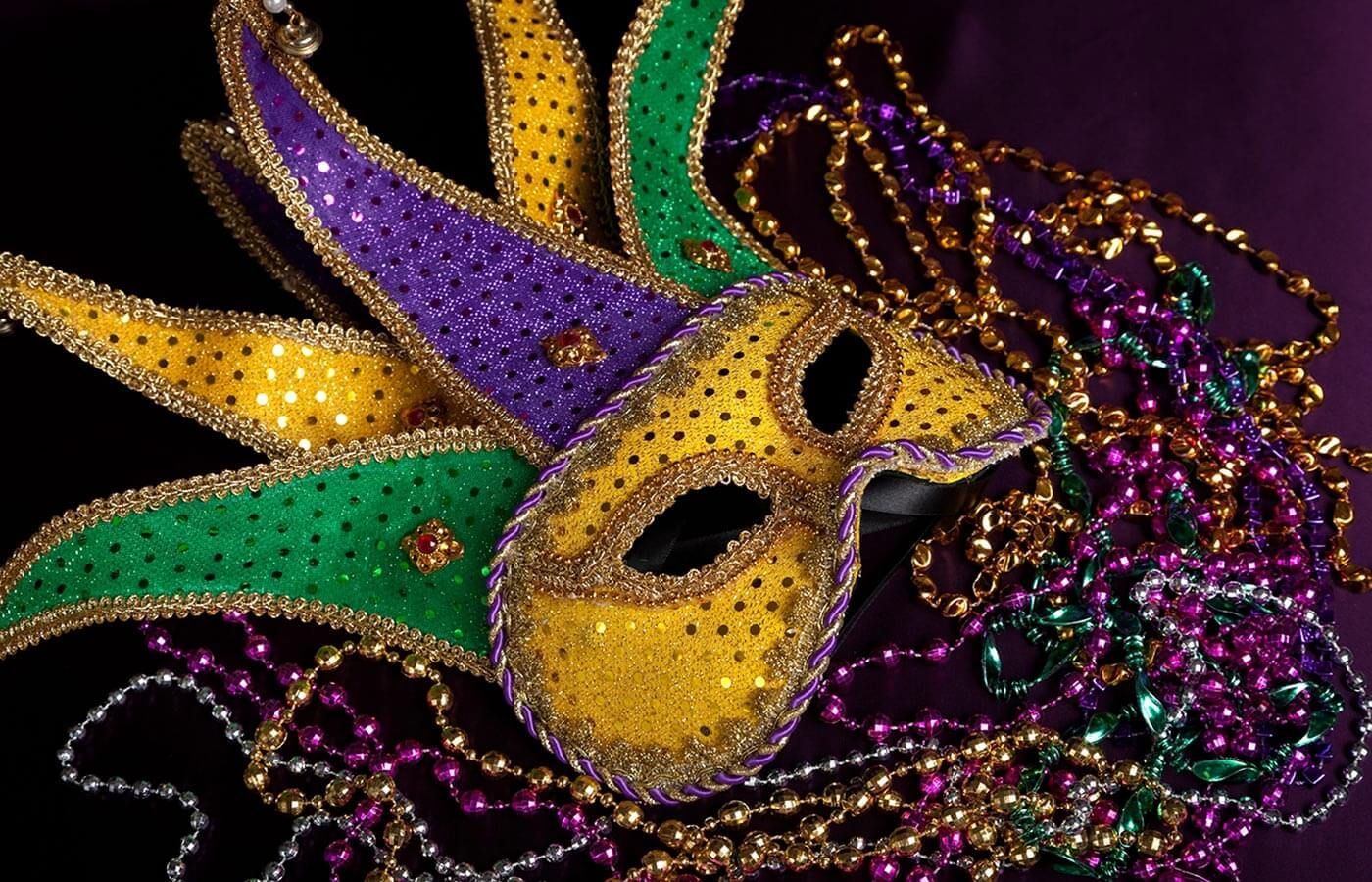Colorful Mardi Gras mask with gold, purple, and green beads and feathers on a black background