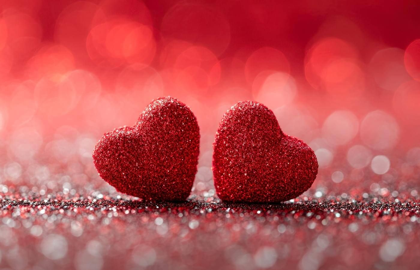 Two red glitter hearts on a sparkling red background