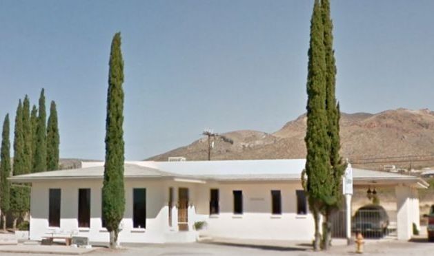 White modern building with tall cypress trees and mountains in the background