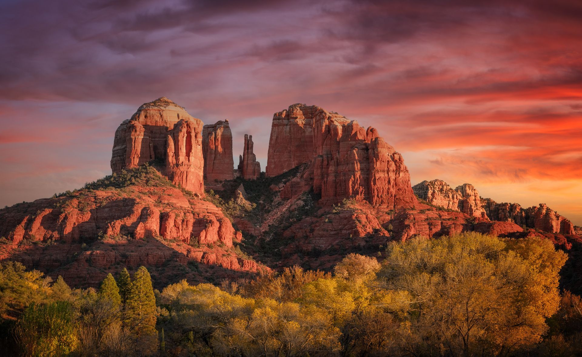 Sunlit red sandstone buttes under a pink-orange sunset sky, framed by autumn trees.