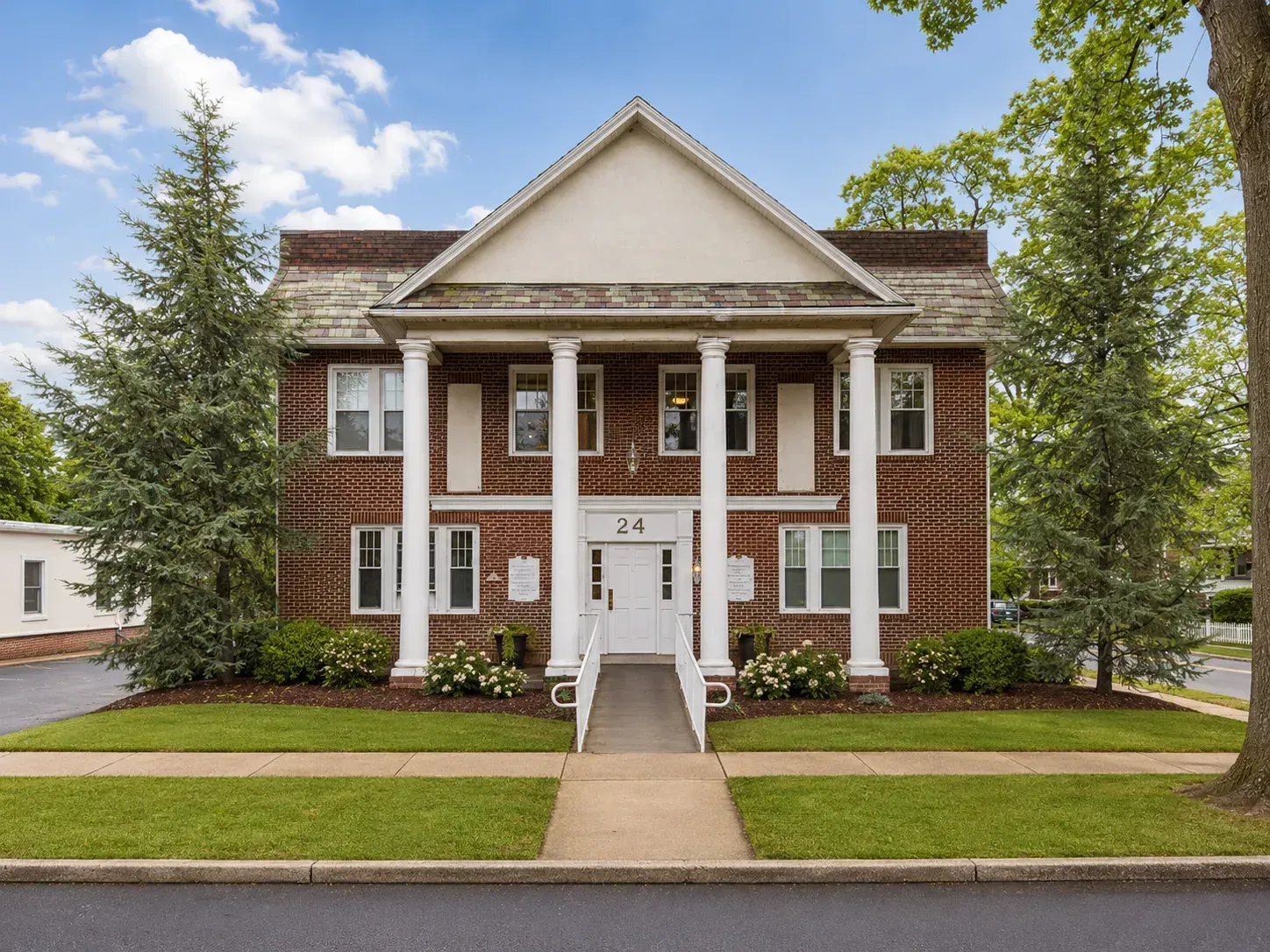Brick two-story house with white columns, front steps, and a central walkway surrounded by green lawn.