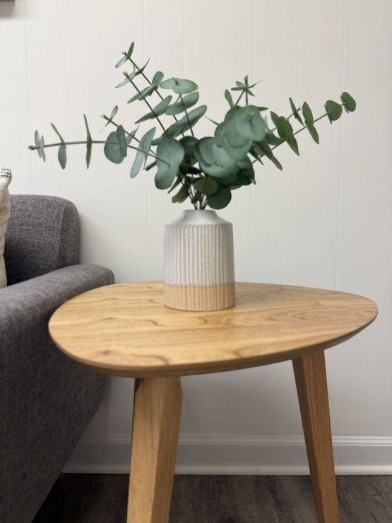 Round wooden side table with a striped vase of eucalyptus in a living room
