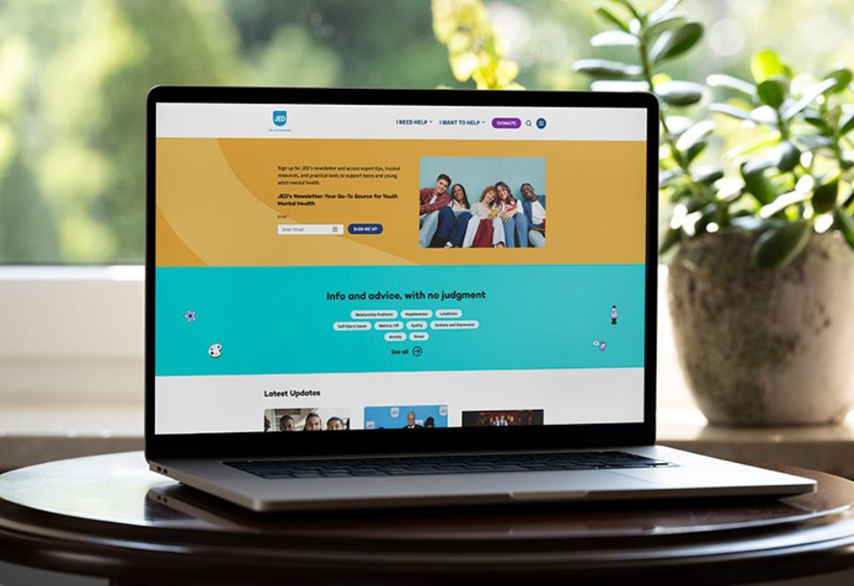 Laptop displaying a colorful website on a round table beside a potted plant