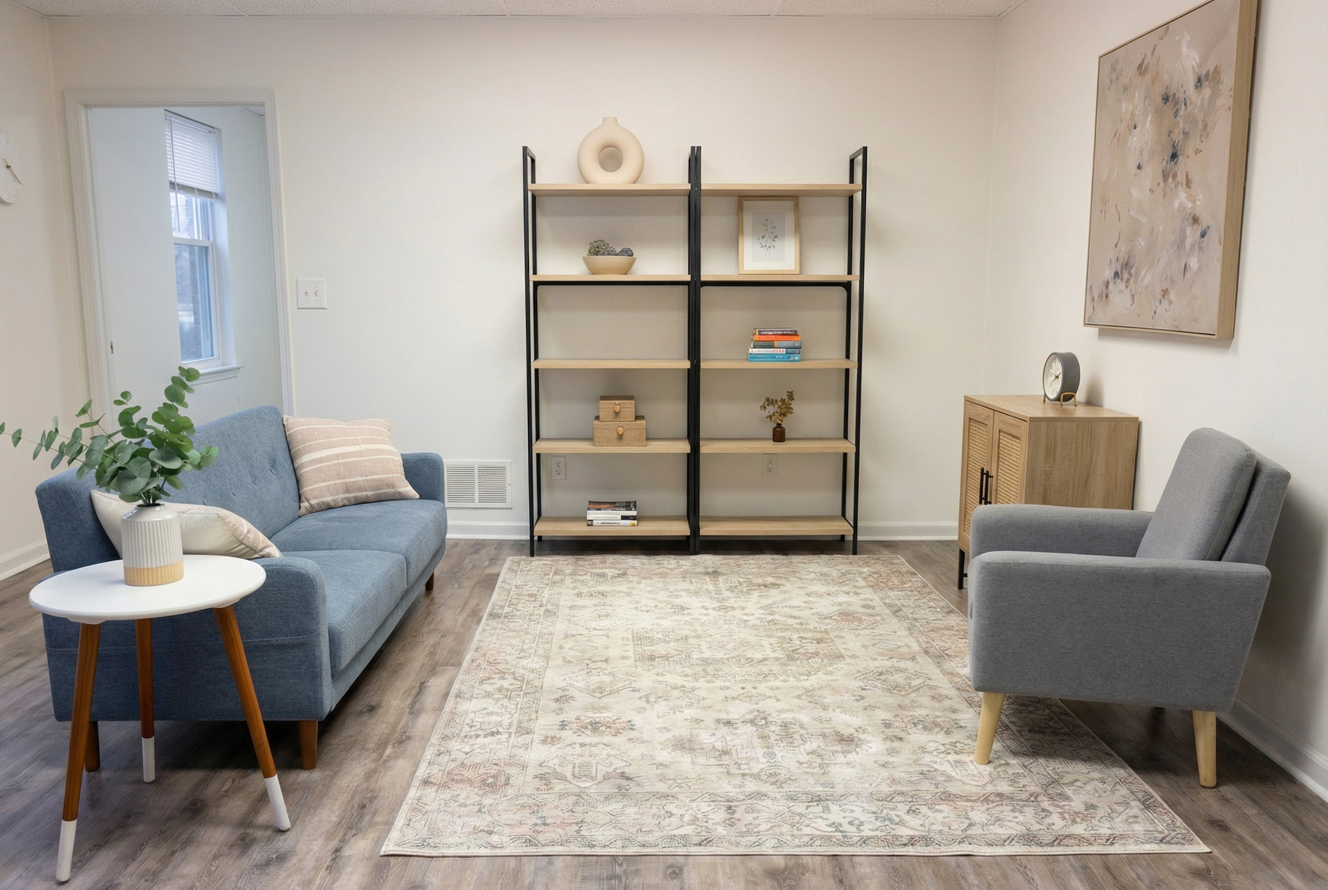Bright living room with blue sofa, gray chair, bookcase, rug, and small table by window