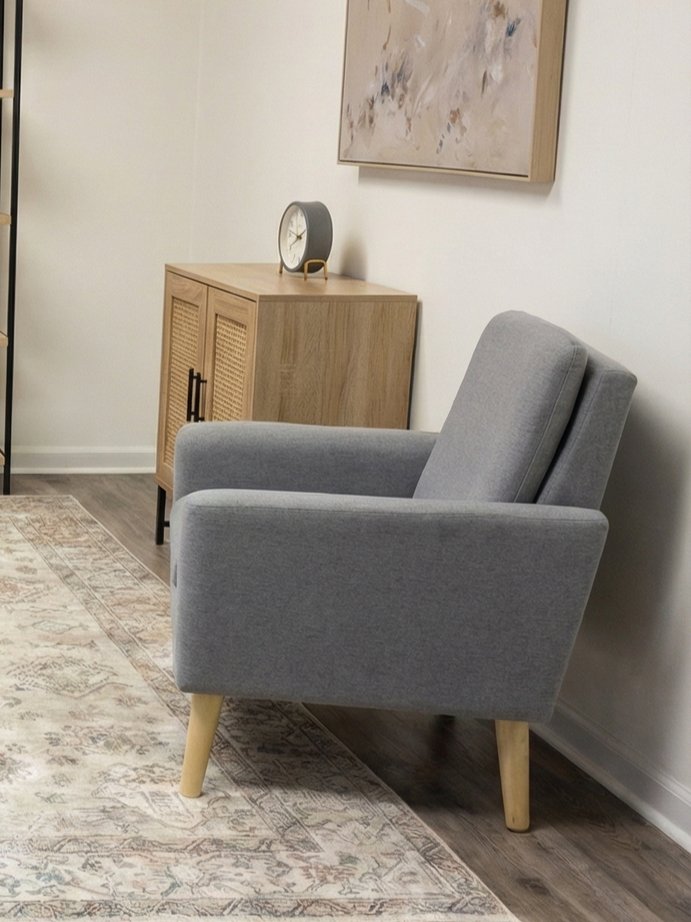 Gray armchair beside a woven cabinet with a clock in a softly lit room