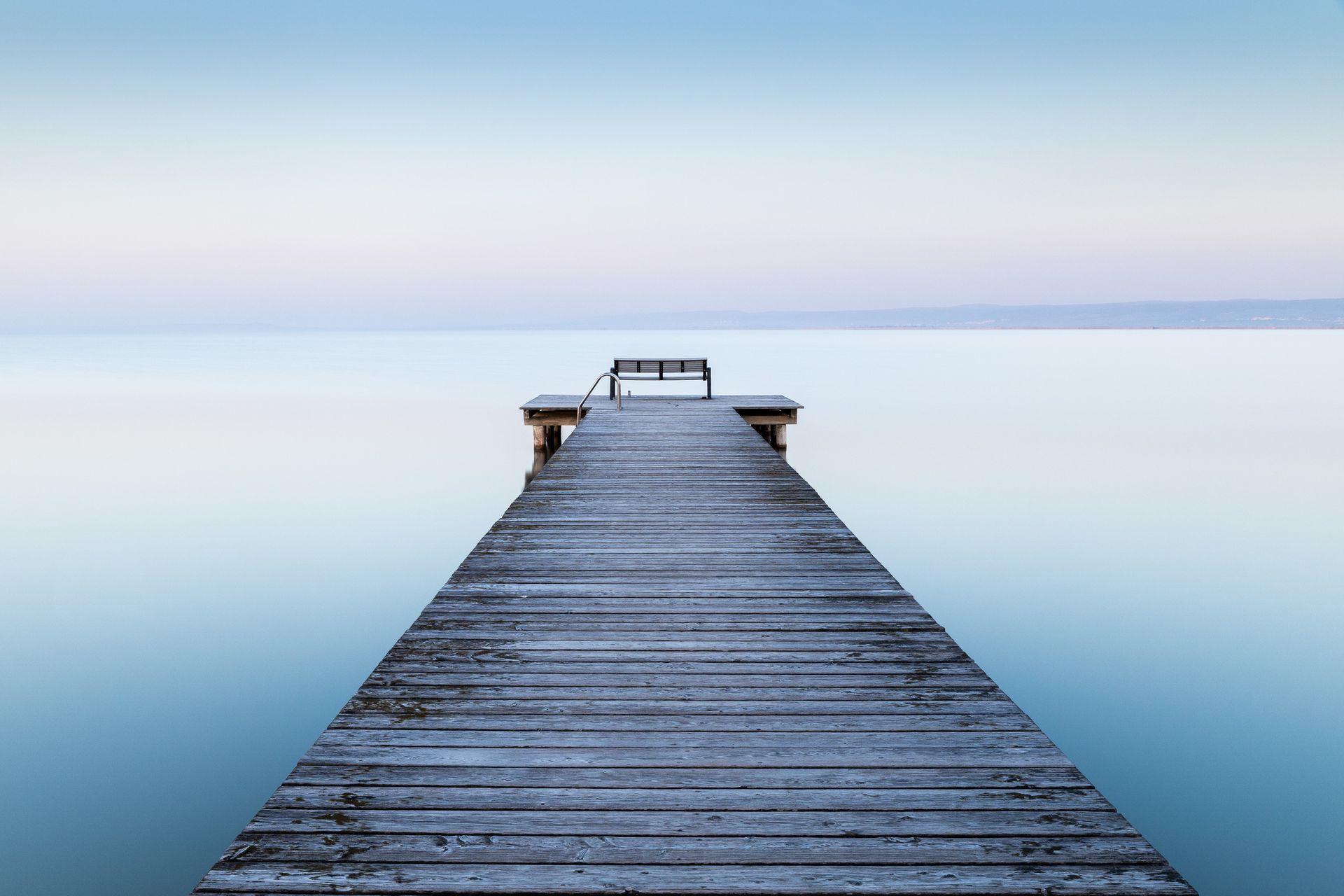 Wooden dock extending into calm blue water under a soft pastel sky