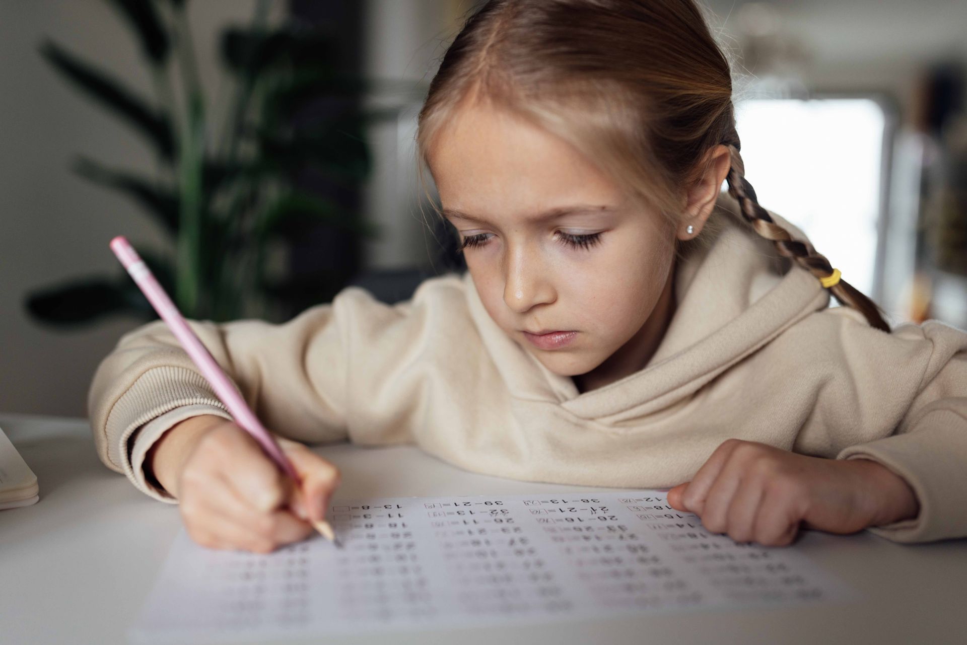 Child writing on a worksheet at a table, focused, with a pencil in a softly lit room