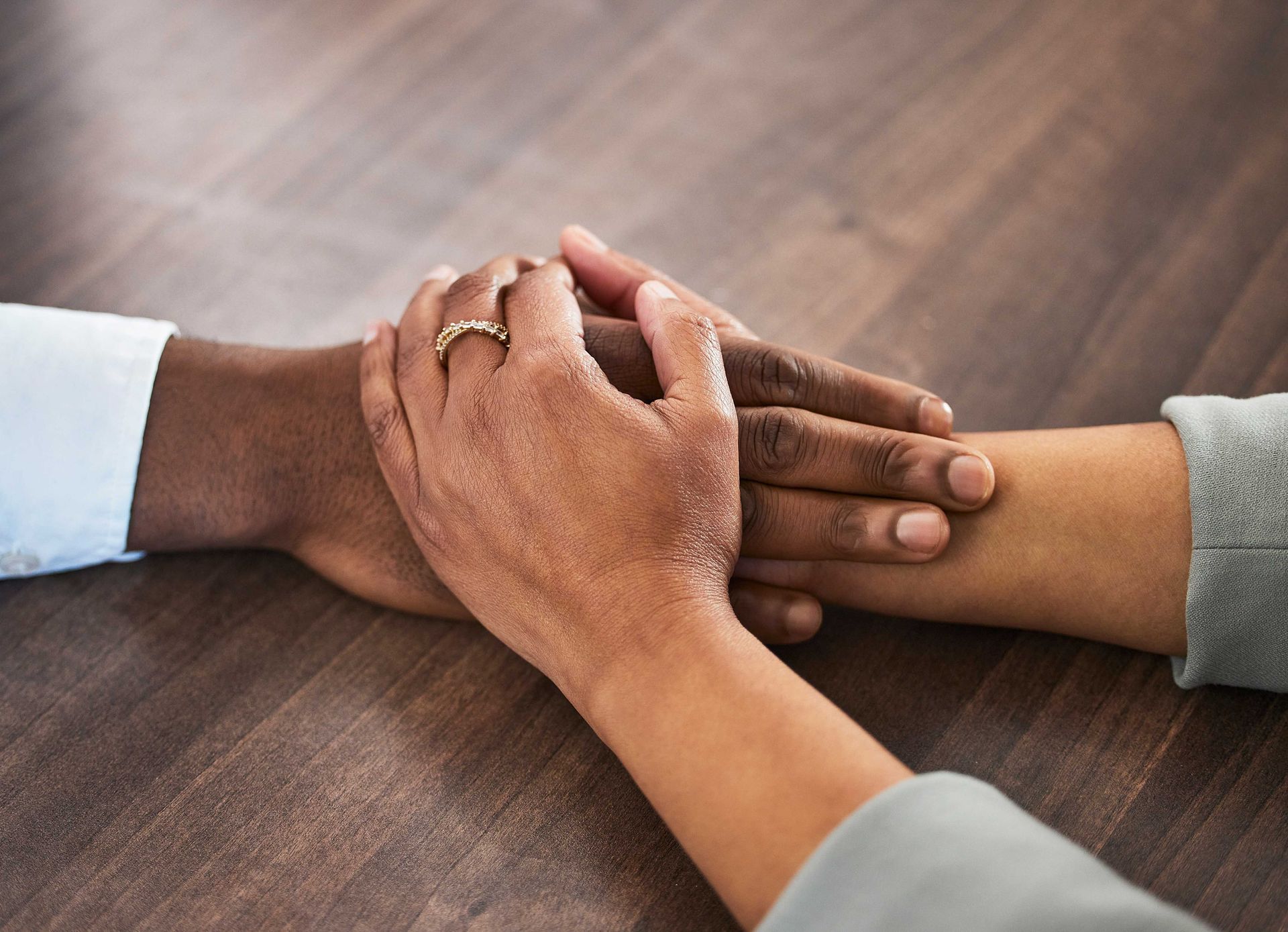 Hands stacked together on a wooden table in a supportive gesture.