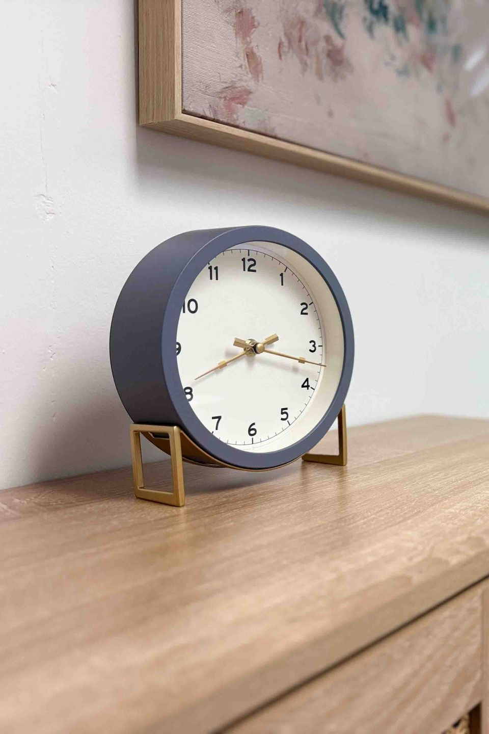 Blue tabletop clock on a wooden dresser beside a framed picture