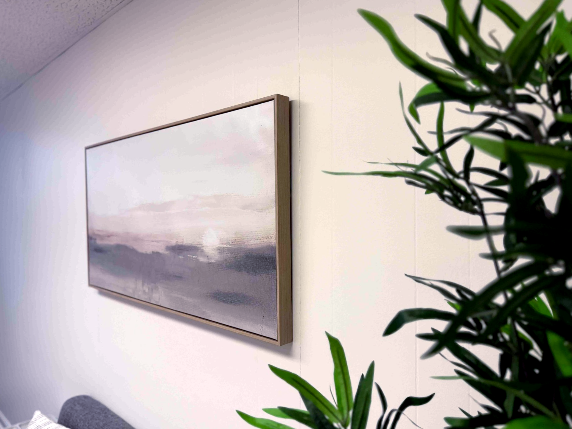 Framed landscape painting on a white wall beside a green potted plant