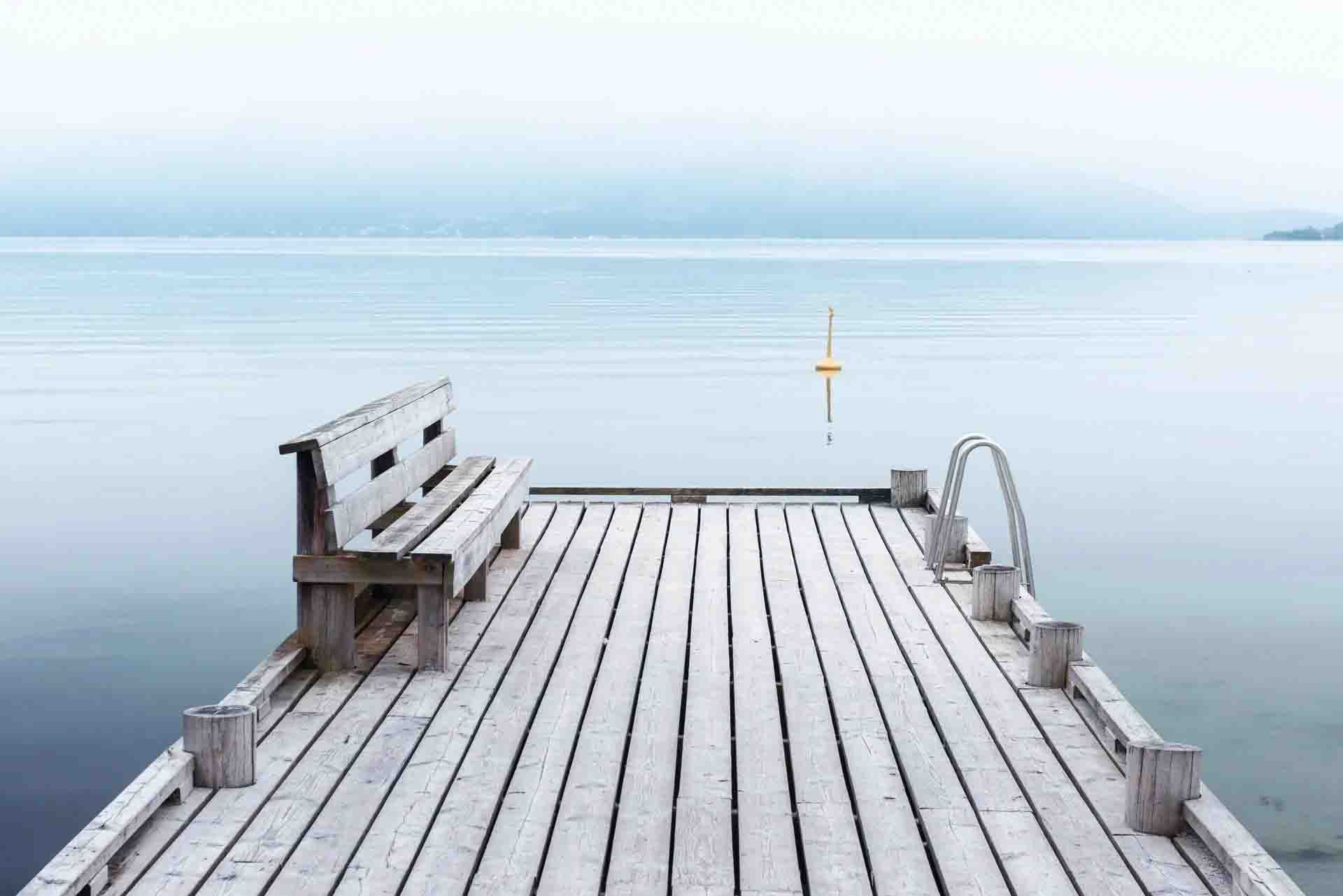 Wooden pier with a bench overlooking a calm, misty lake under a pale sky
