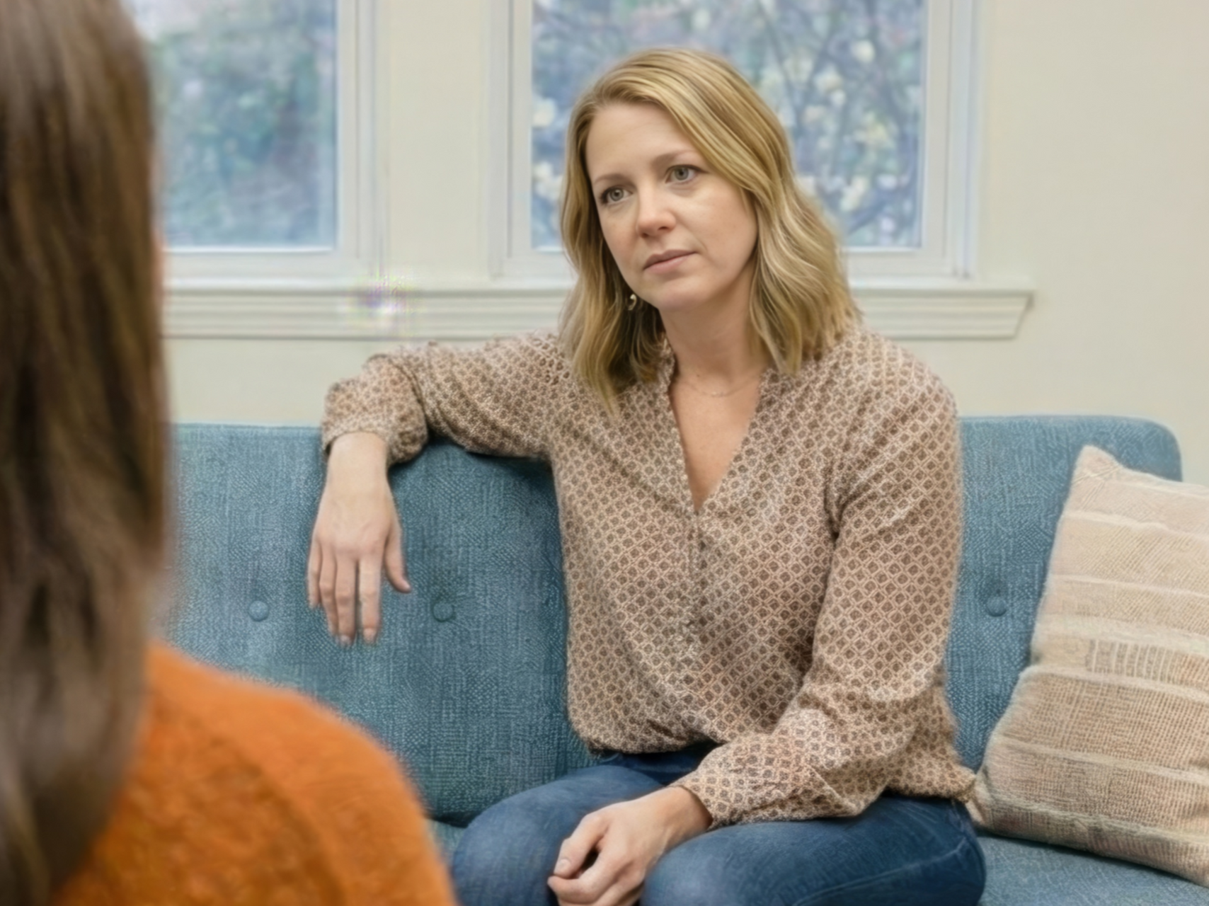 Woman listening on a blue couch in a bright room, facing someone off-camera.