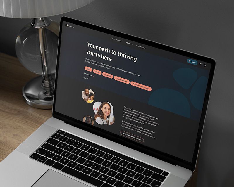 Laptop on a desk displaying a dark website mockup titled “Your path to thriving,” beside a lamp and glass lamp base