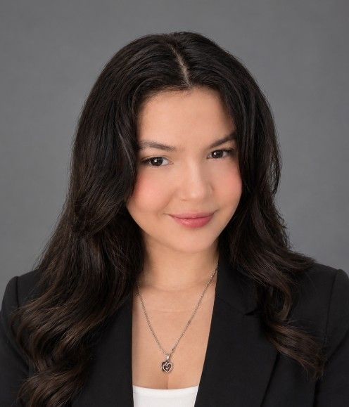 Woman in a blazer and white shirt smiles at the camera against a light blue background.