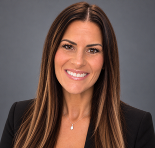 Woman in a blazer and white shirt smiles at the camera against a light blue background.