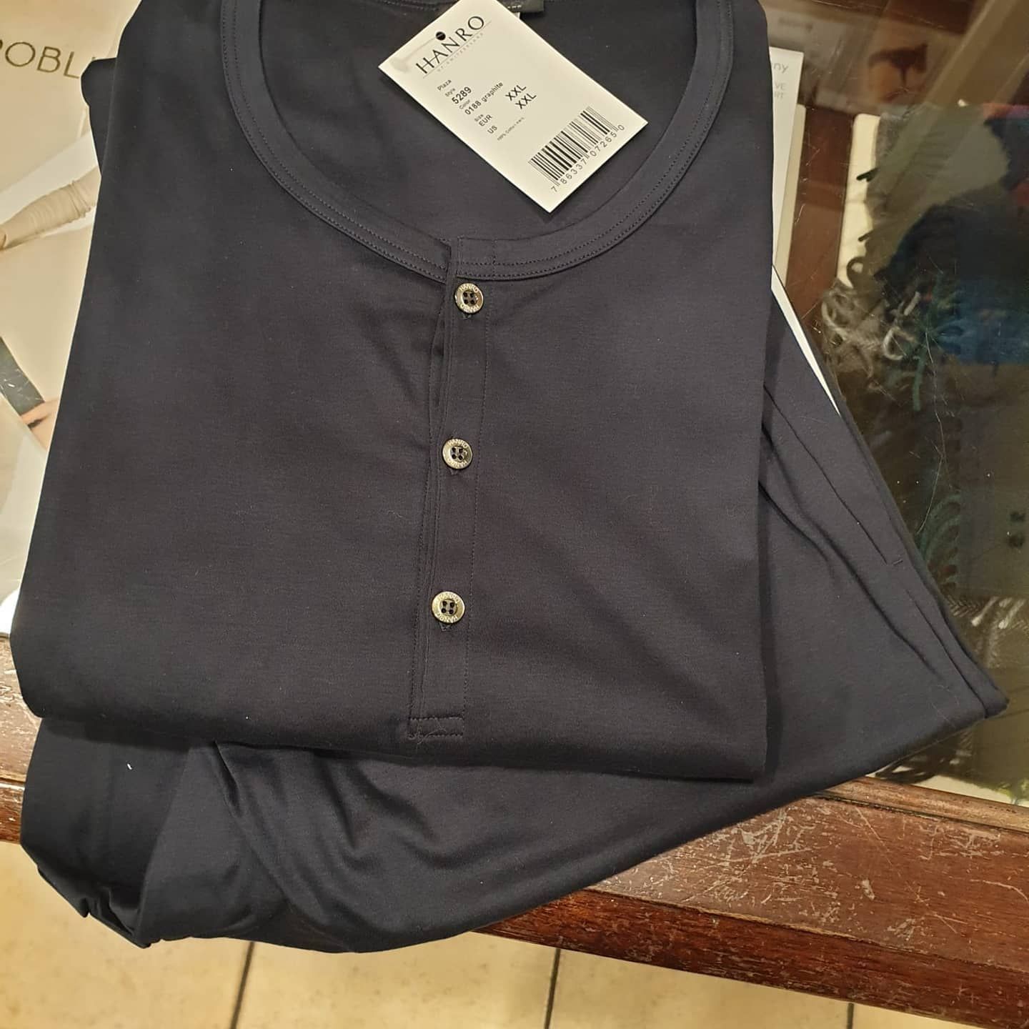 Pigiama da uomo blu scuro, piegato su un tavolo. Si vede una maglia con bottoni e un'etichetta.
