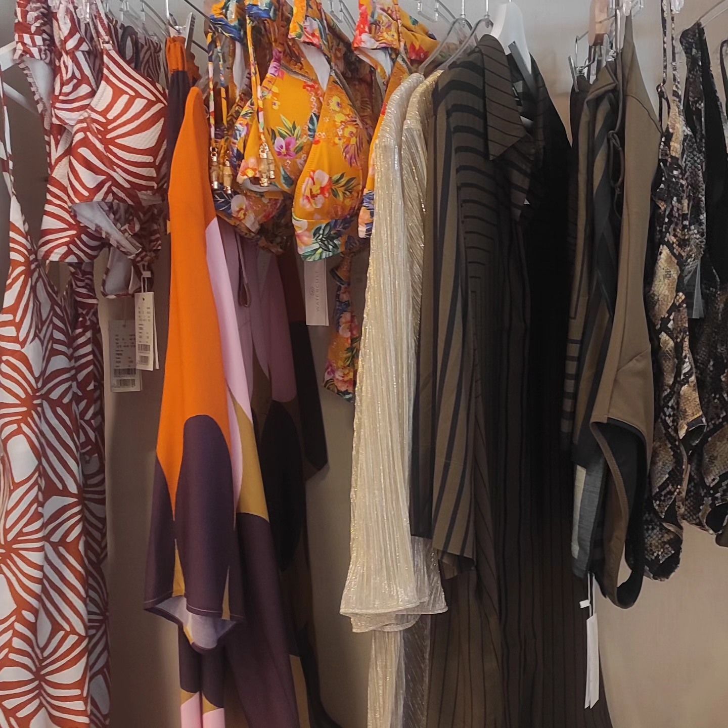 Vestiti appesi su un appendiabiti. Abiti, top e costumi da bagno di vari colori.