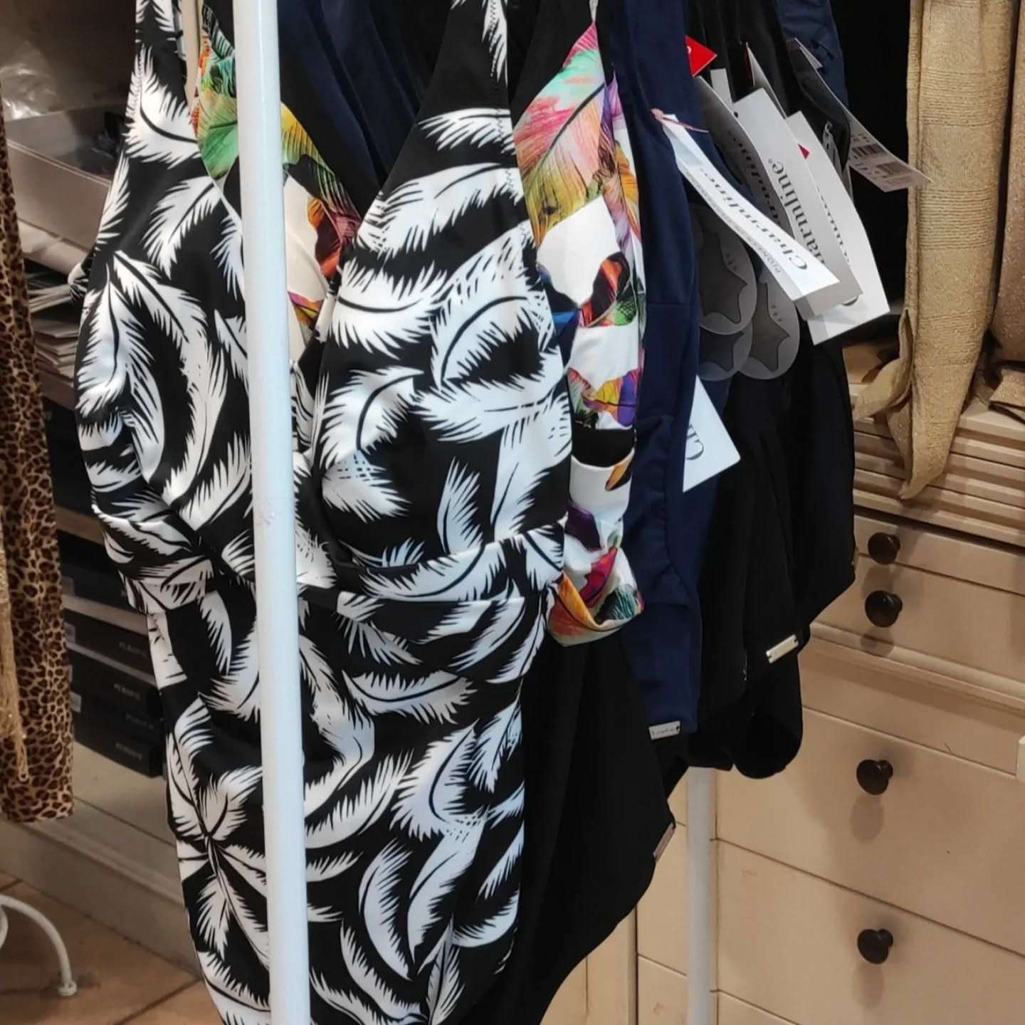 Costumi da bagno appesi su un appendiabiti bianco, vari modelli e colori.
