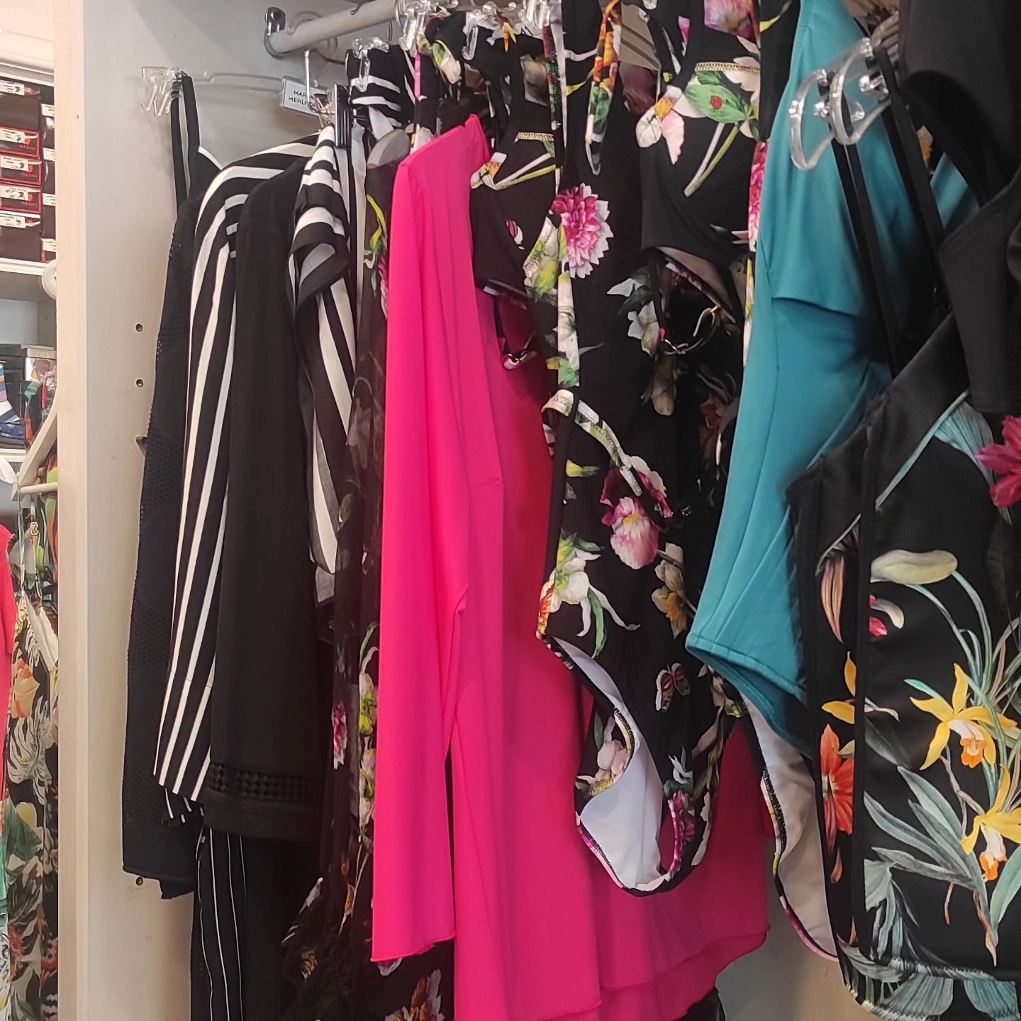 Appendiabiti con top a righe bianche e nere, blazer rosa, abiti floreali e in tinta unita.