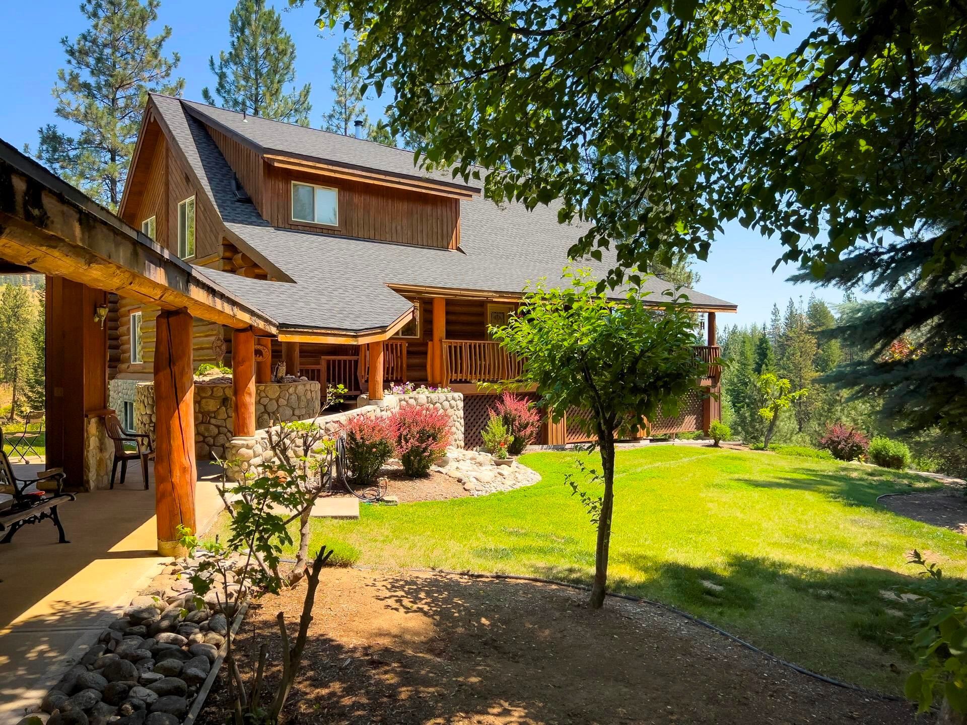 Rustic house with a porch, green lawn, trees, and bright sunlight in a garden setting