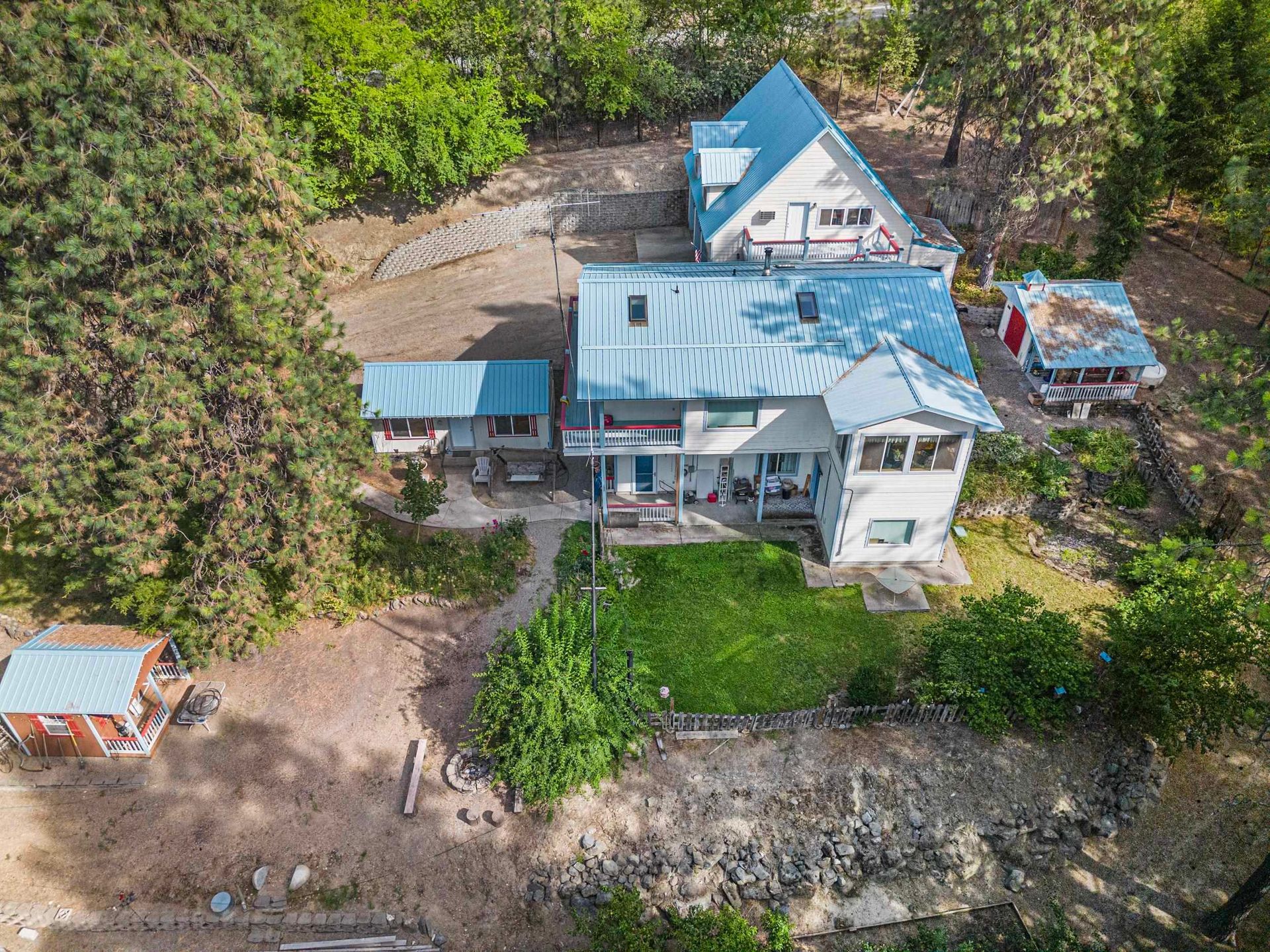 Aerial view of a blue-roofed house surrounded by trees near a rocky shoreline