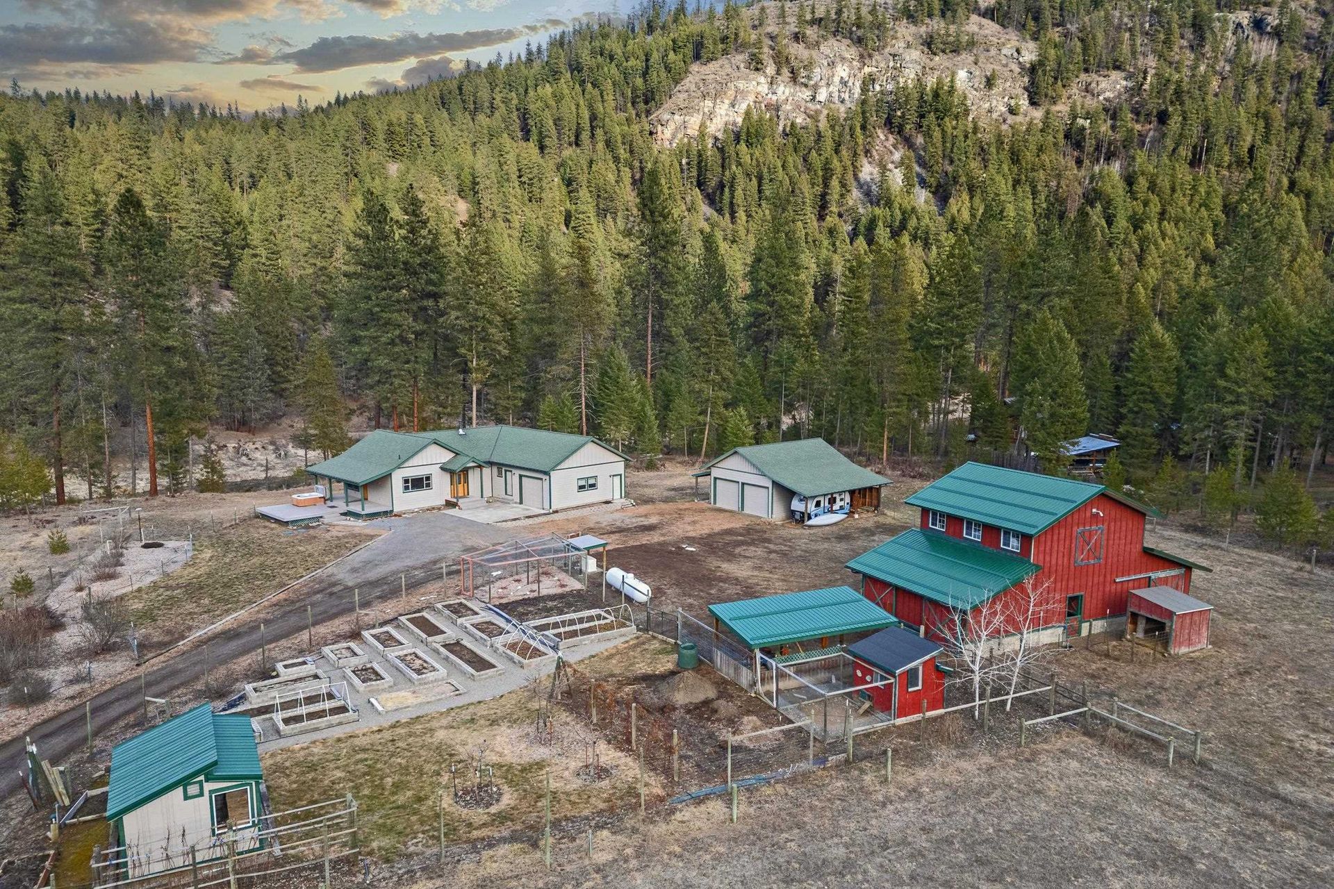 Rural mountain homestead with red and teal cabins beside a pine forest and rocky terrain