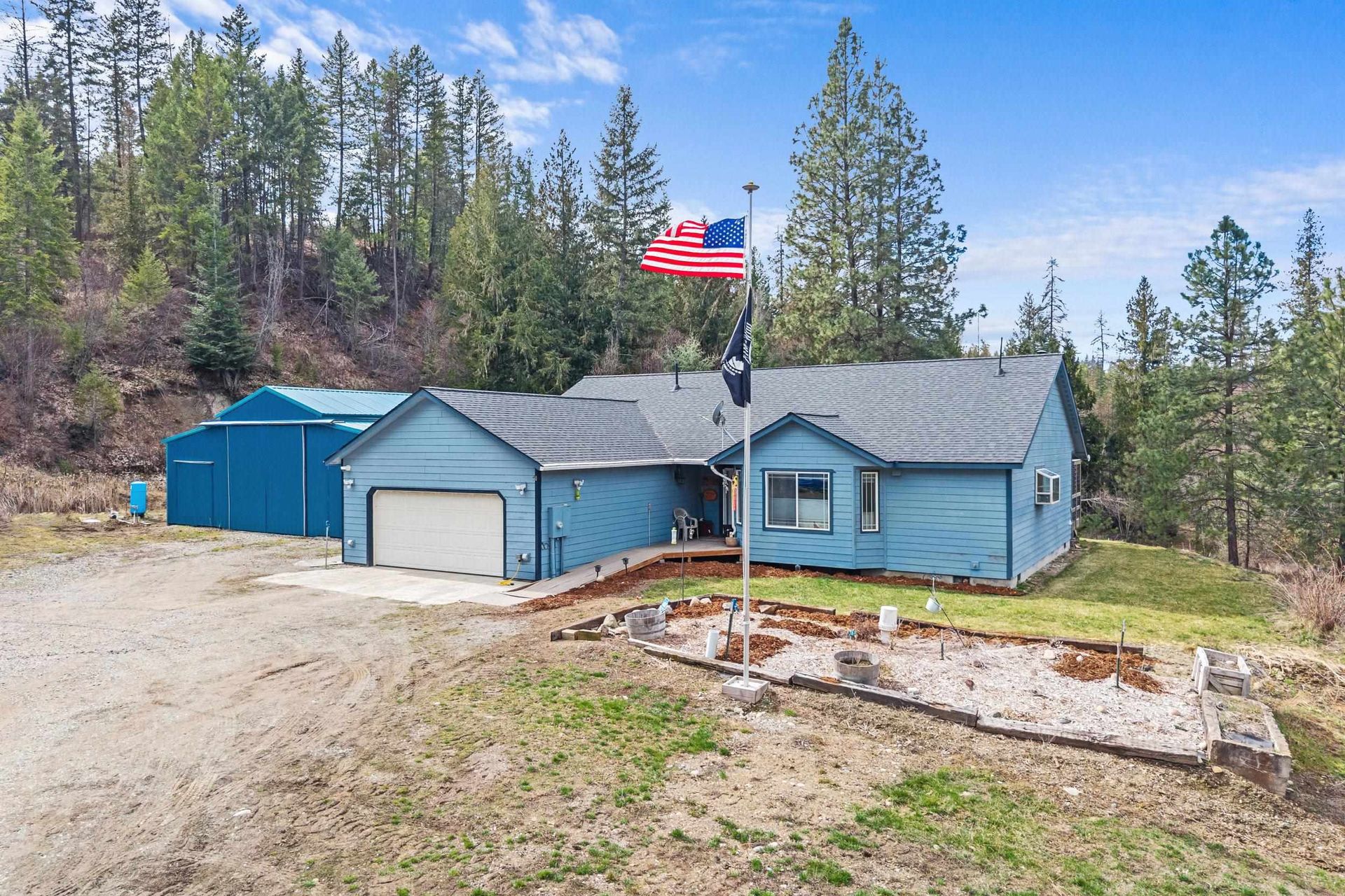 Blue house with attached garage and American flag on a rural wooded lot