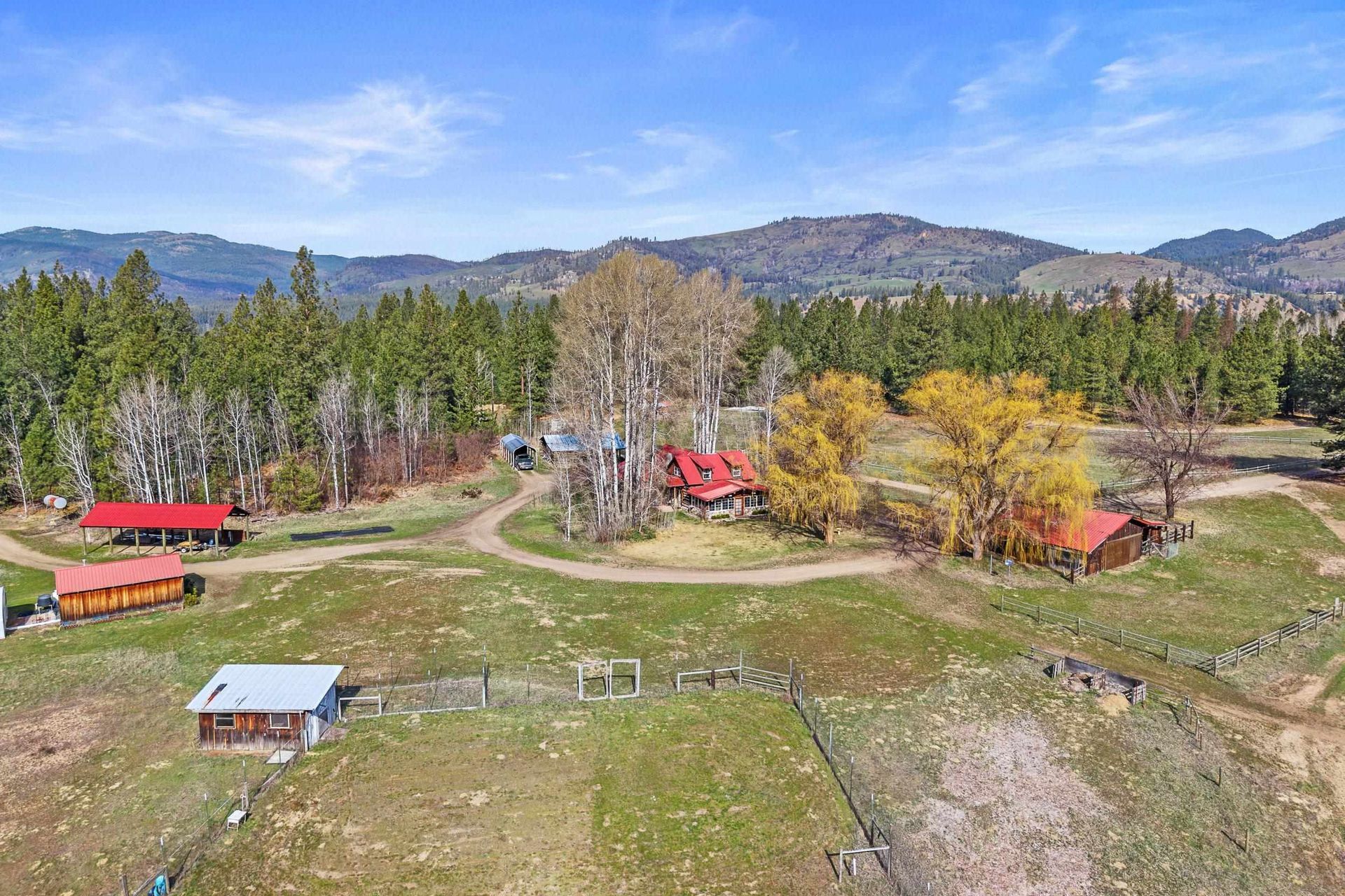 Rural property with red-roofed buildings, trees, open pasture, and distant mountains under a clear sky