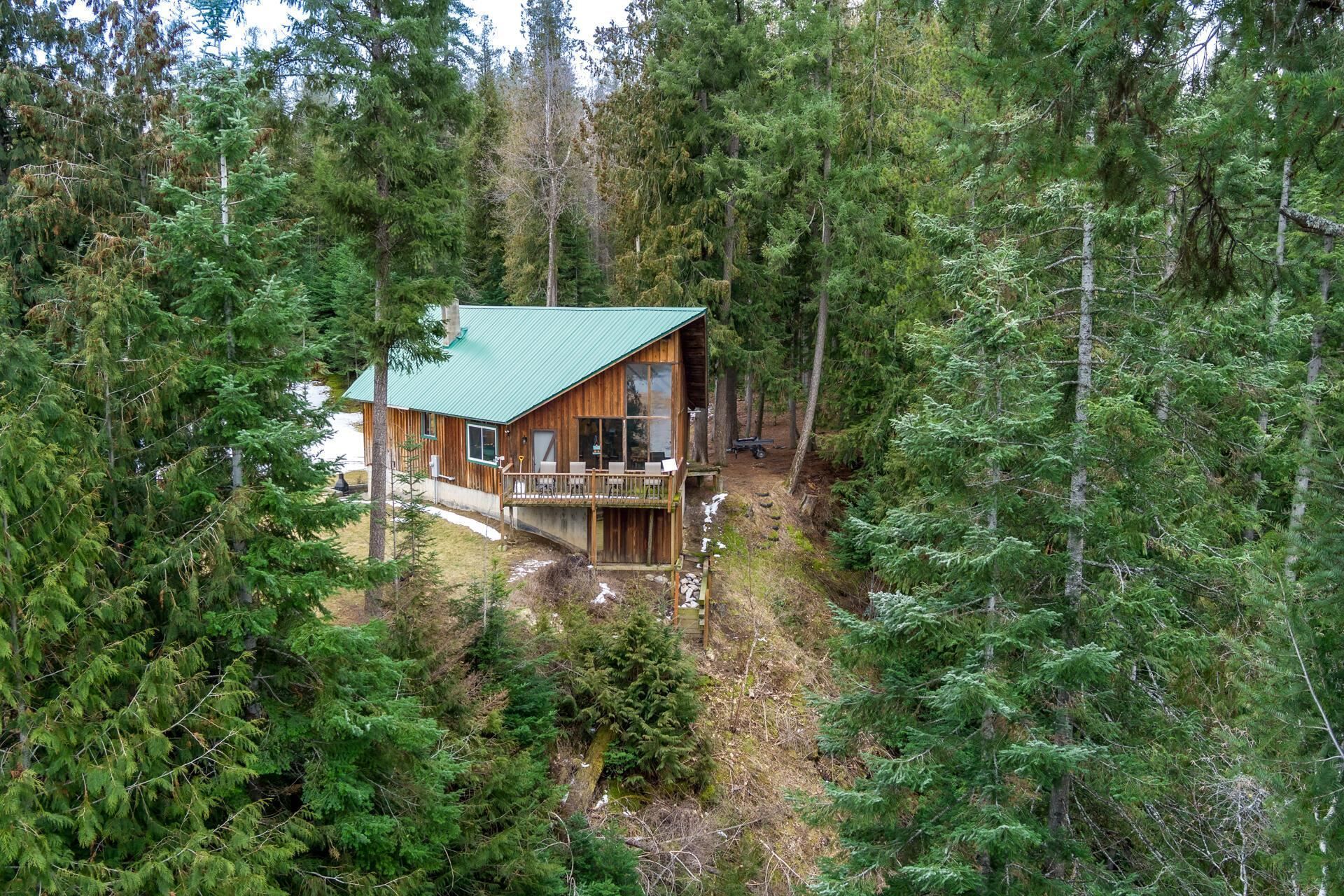 Cabin with a green roof nestled among dense evergreen trees on a forested hillside