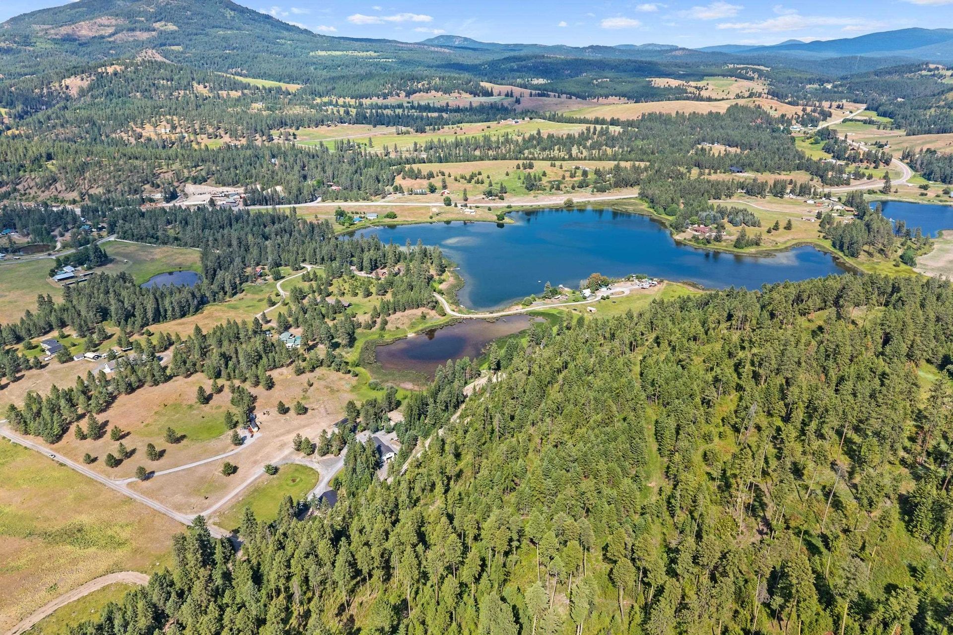 Aerial view of a blue lake surrounded by green forested hills and open fields