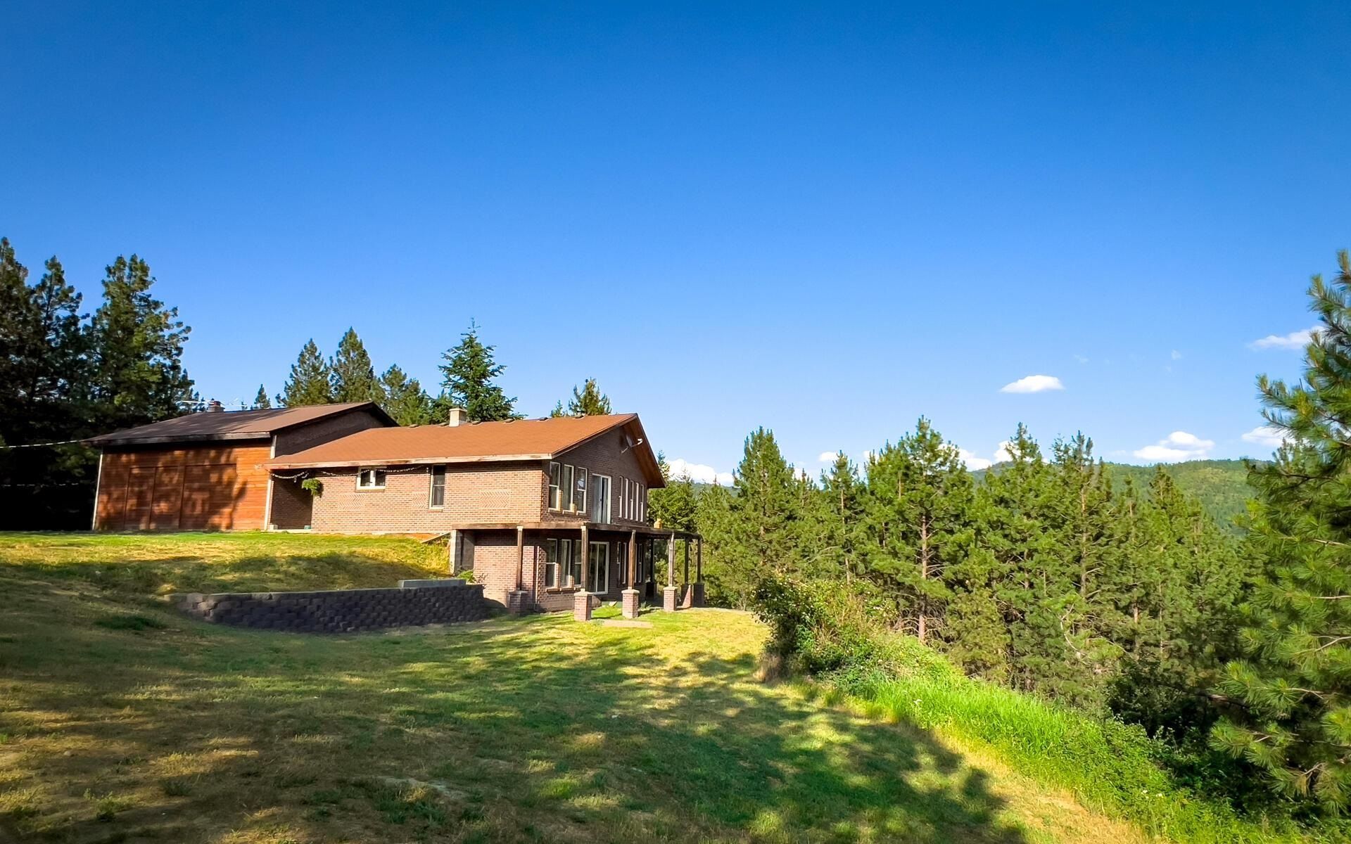 Wooden house on a grassy hillside with pine trees under a clear blue sky