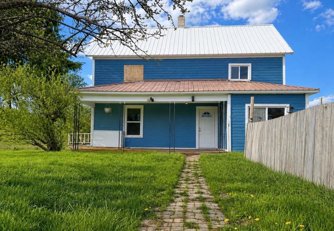 Blue two-story house with white trim, front lawn, and brick walkway under a partly cloudy sky
