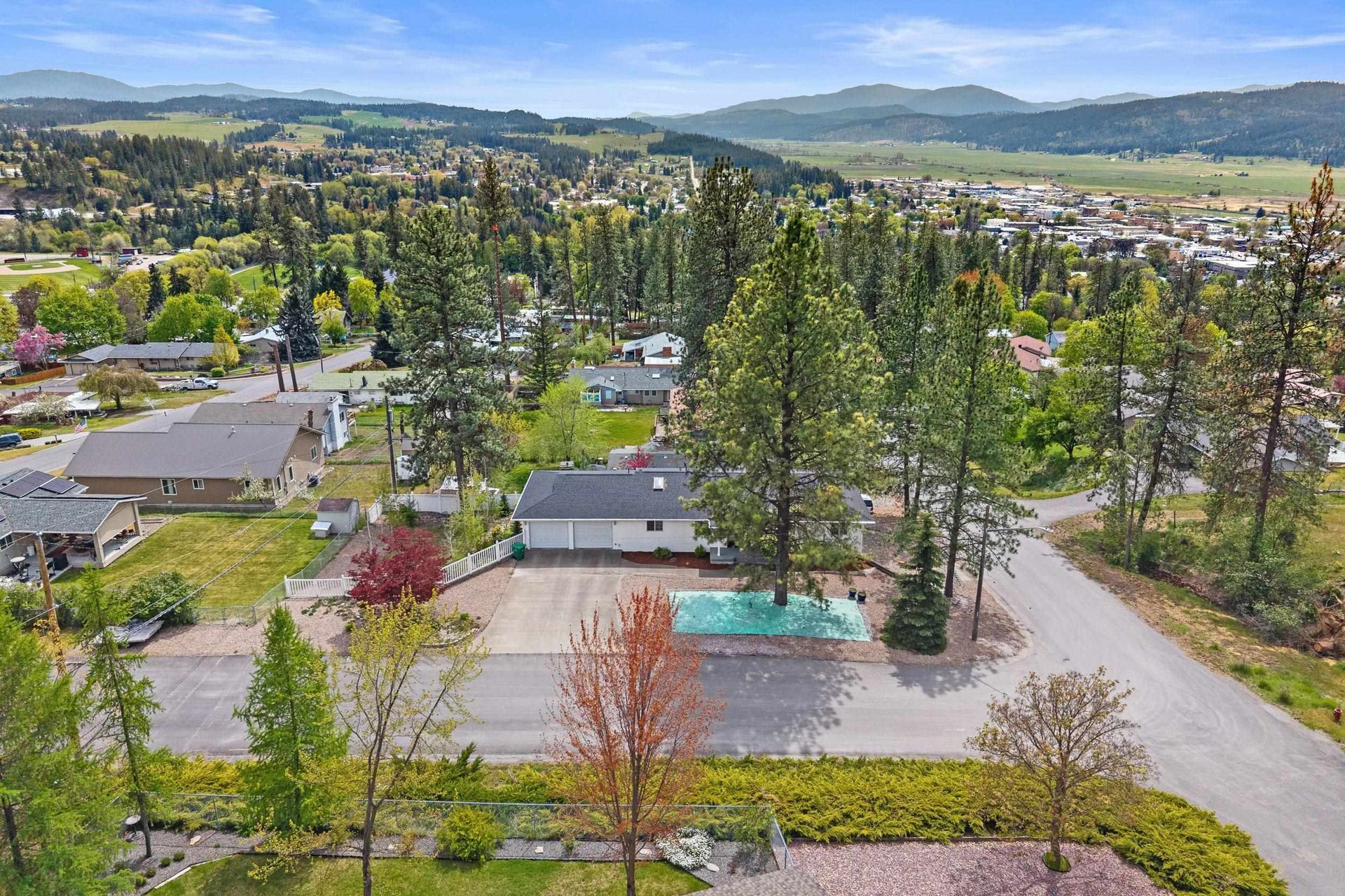 Aerial view of a wooded neighborhood with homes, roads, and mountains in the distance.