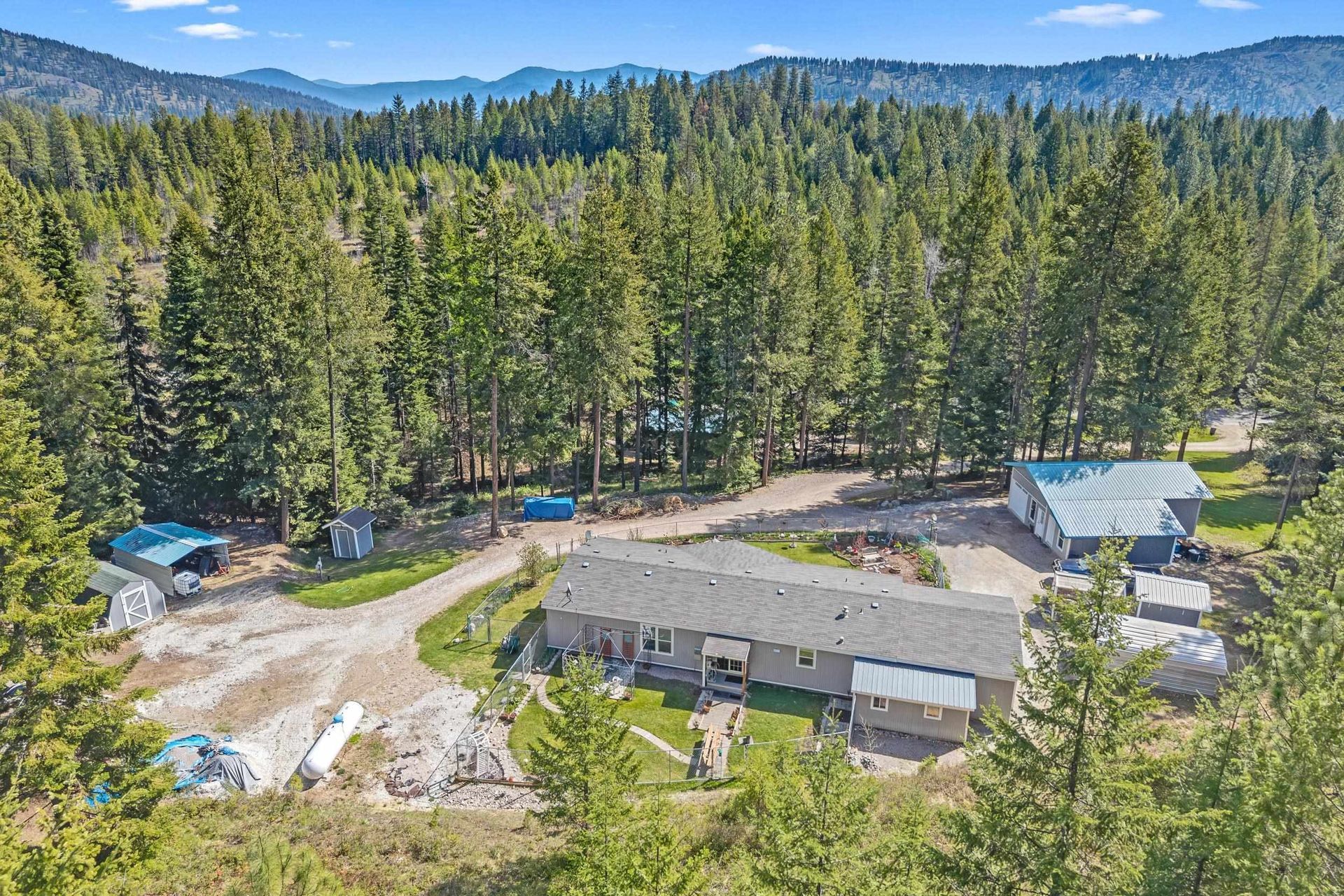 Aerial view of a forested mountain lodge with cabins, dirt roads, and parked vehicles.