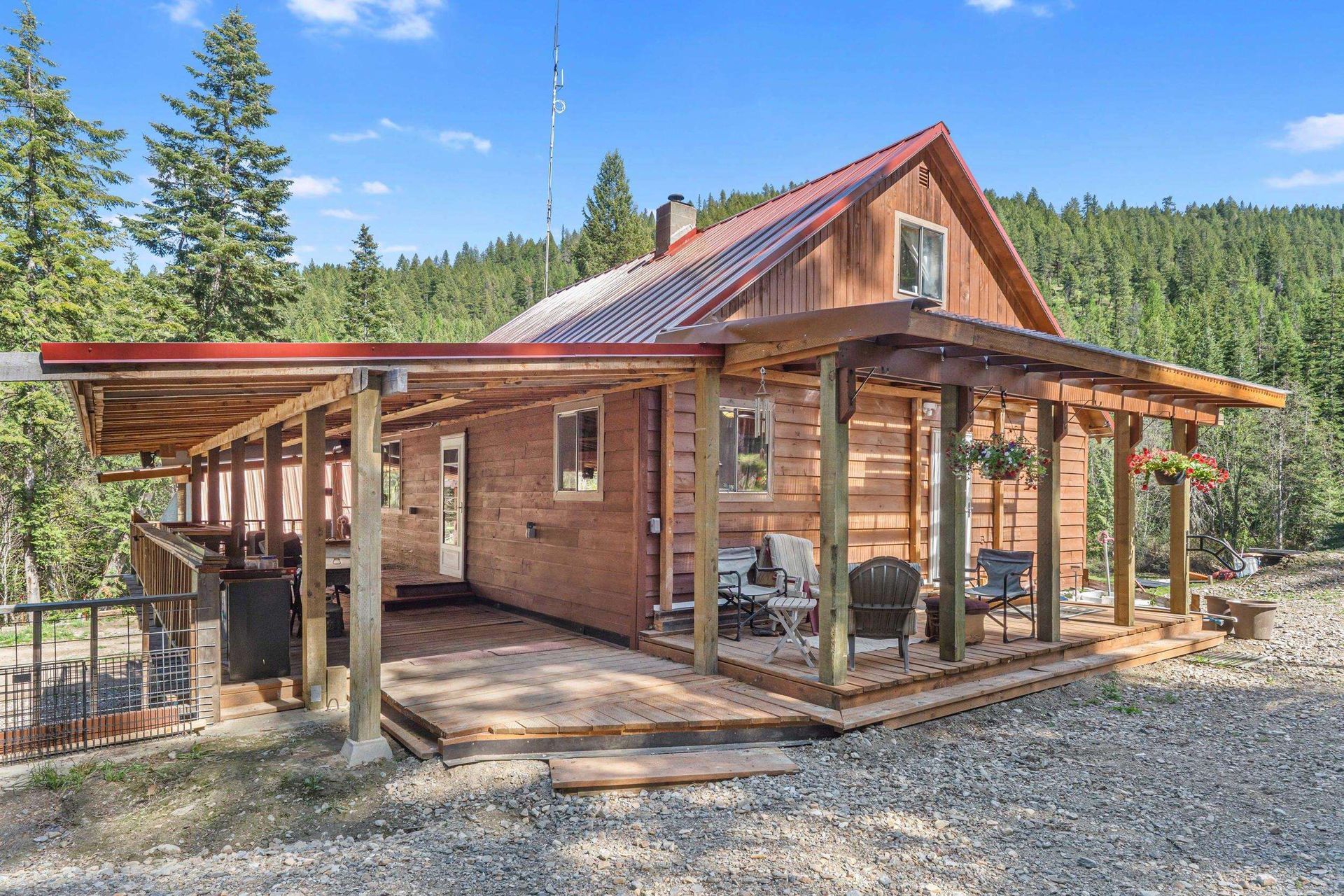Rustic cabin with a covered porch and red metal roof in a wooded mountain setting