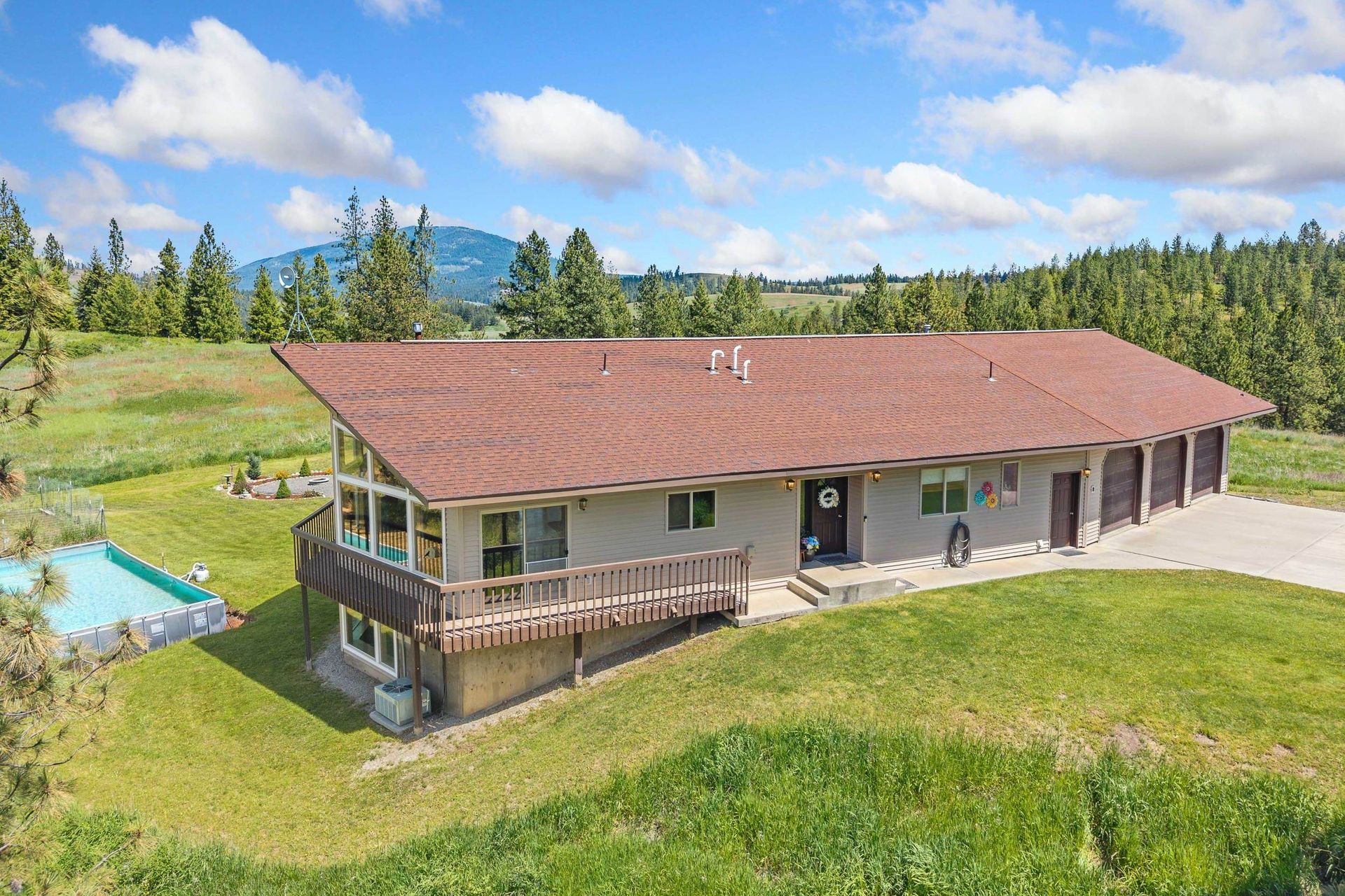 Rural house with red roof, wraparound deck, and grassy yard with mountains in the background