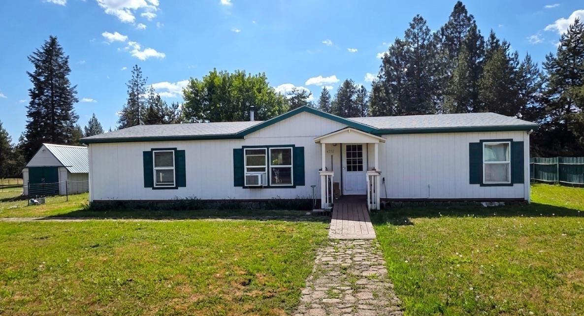Single-story white house with green shutters and a front walkway under a sunny sky