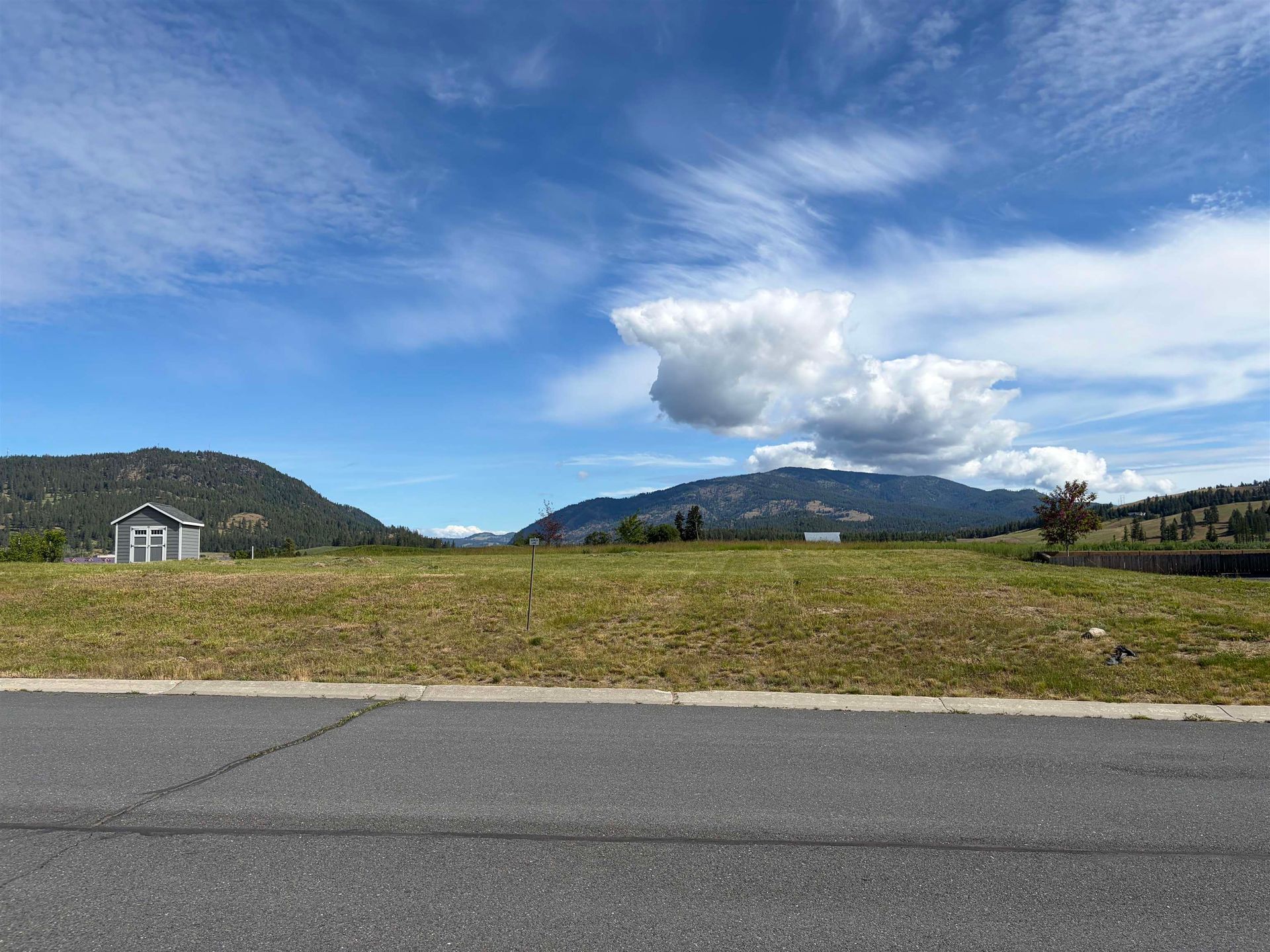 Wide mountain landscape with blue sky, white clouds, grassy field, and road in the foreground