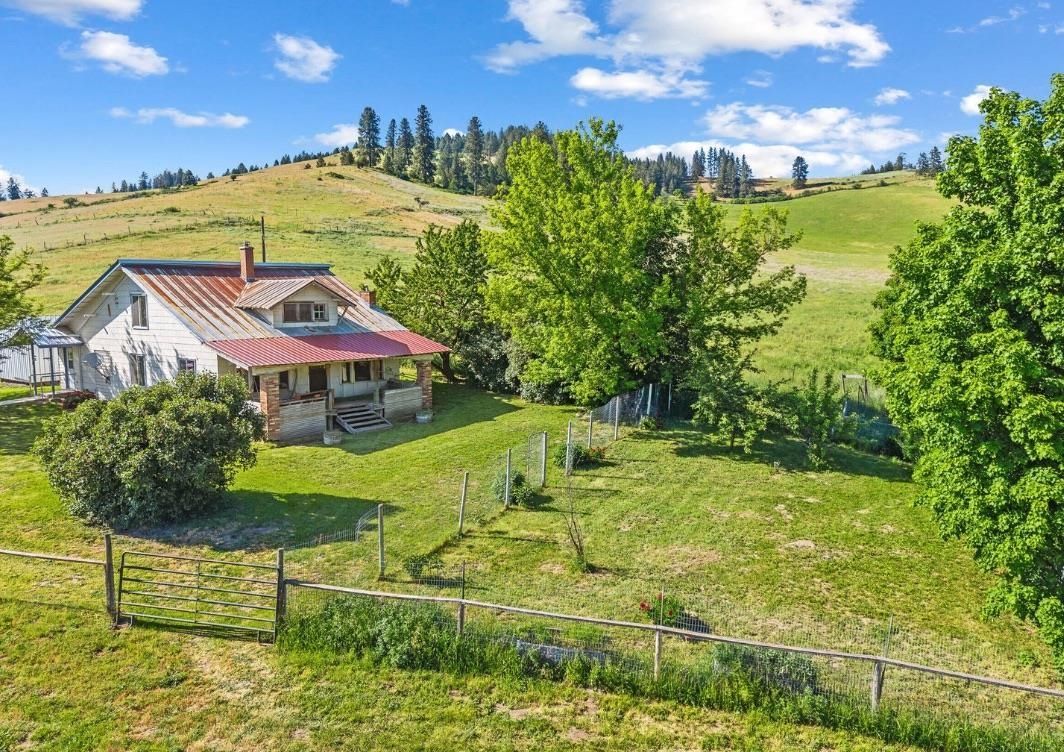Rural farmhouse with red roof on a green hillside under a bright blue sky