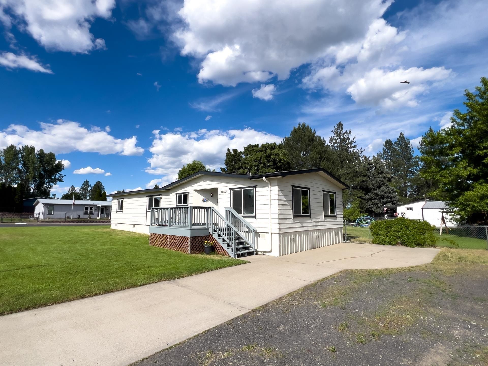 Small white mobile home with steps on a grassy lot under a partly cloudy blue sky.