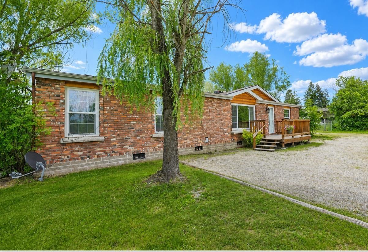 Brick house with white trim, front porch, tree, green lawn, and gravel driveway under a blue sky