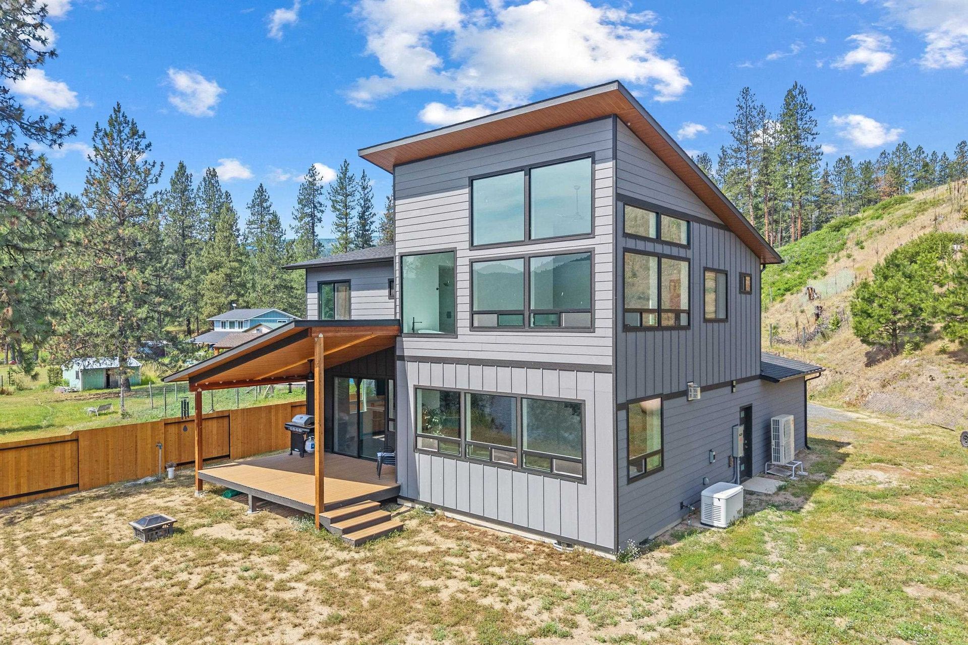Modern gray two-story house with wood accents and large windows on a wooded hillside.