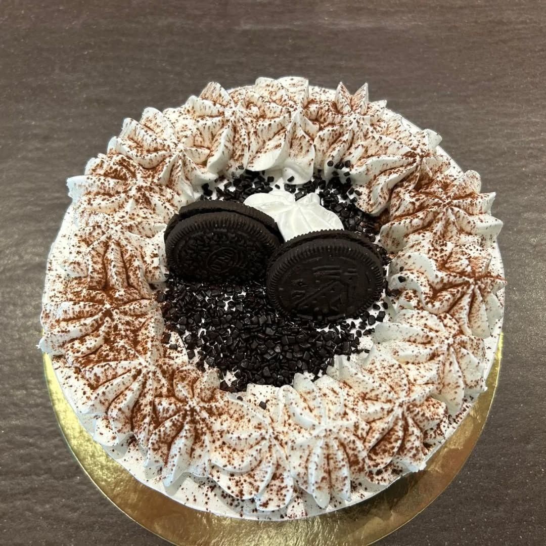 Torta al cioccolato decorata con ciuffi di panna montata e due biscotti Oreo in cima.
