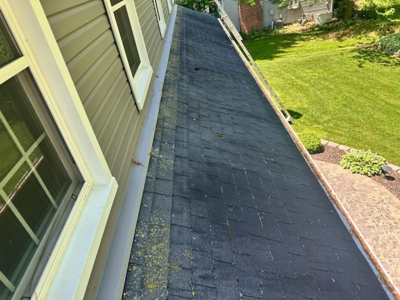 Dark shingled roof with moss, next to siding with windows. View overlooks a lawn.