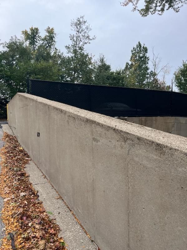 Concrete ramp leading up to a dark structure, with trees in the background and fall leaves nearby.