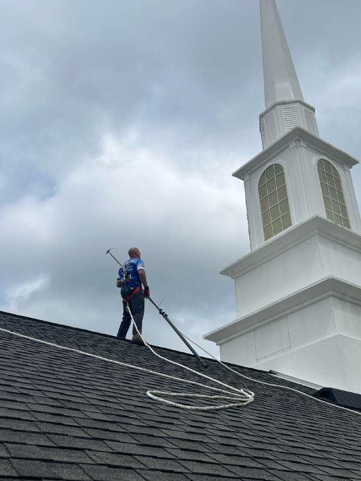 A person on a church roof with equipment, working near the steeple. Overcast sky.
